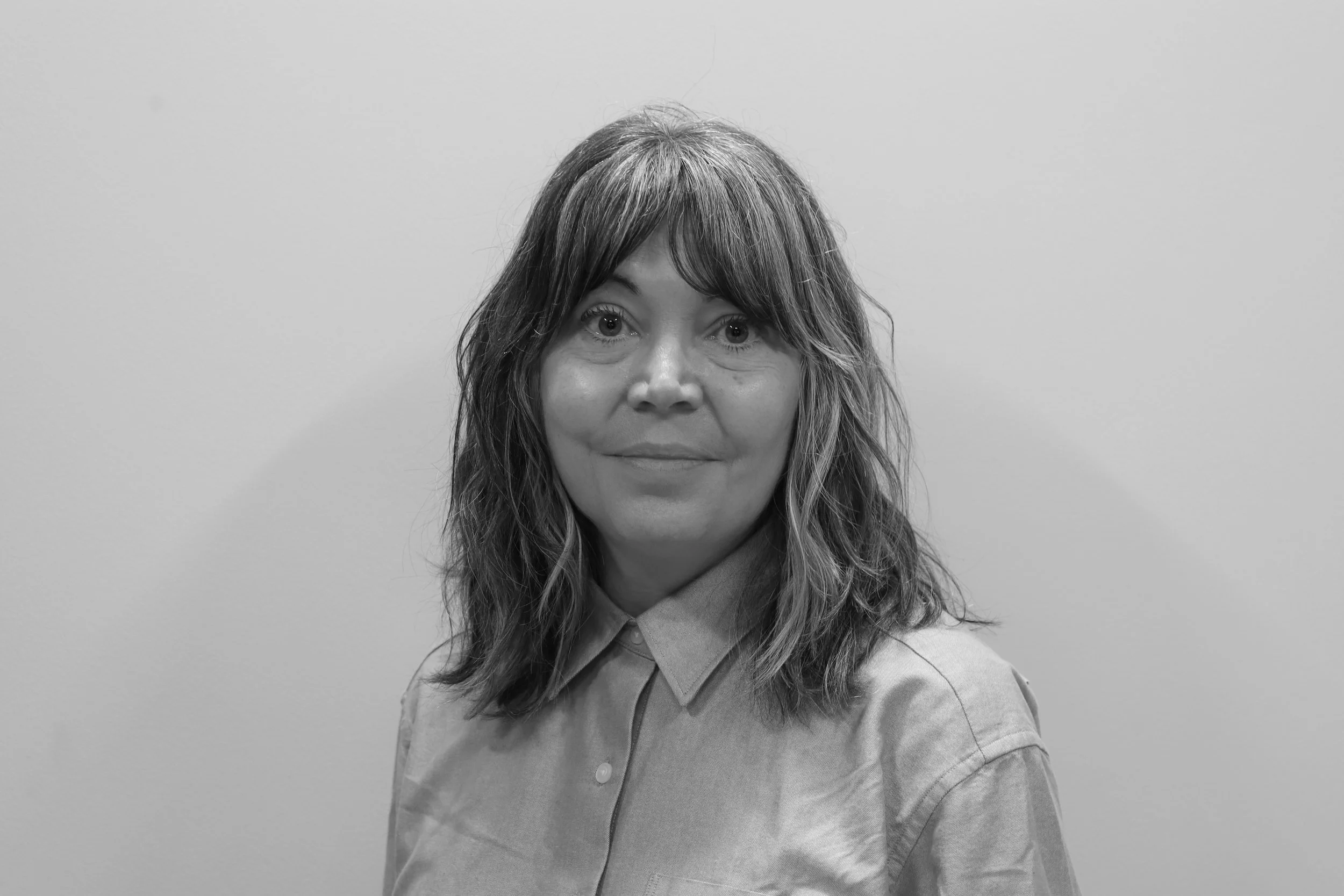 Anne Rhind, CEO of Greater Manchester Mayor's Charity. A woman with dark, wavy hair wearing a floral-patterned blouse stands against a plain wall.