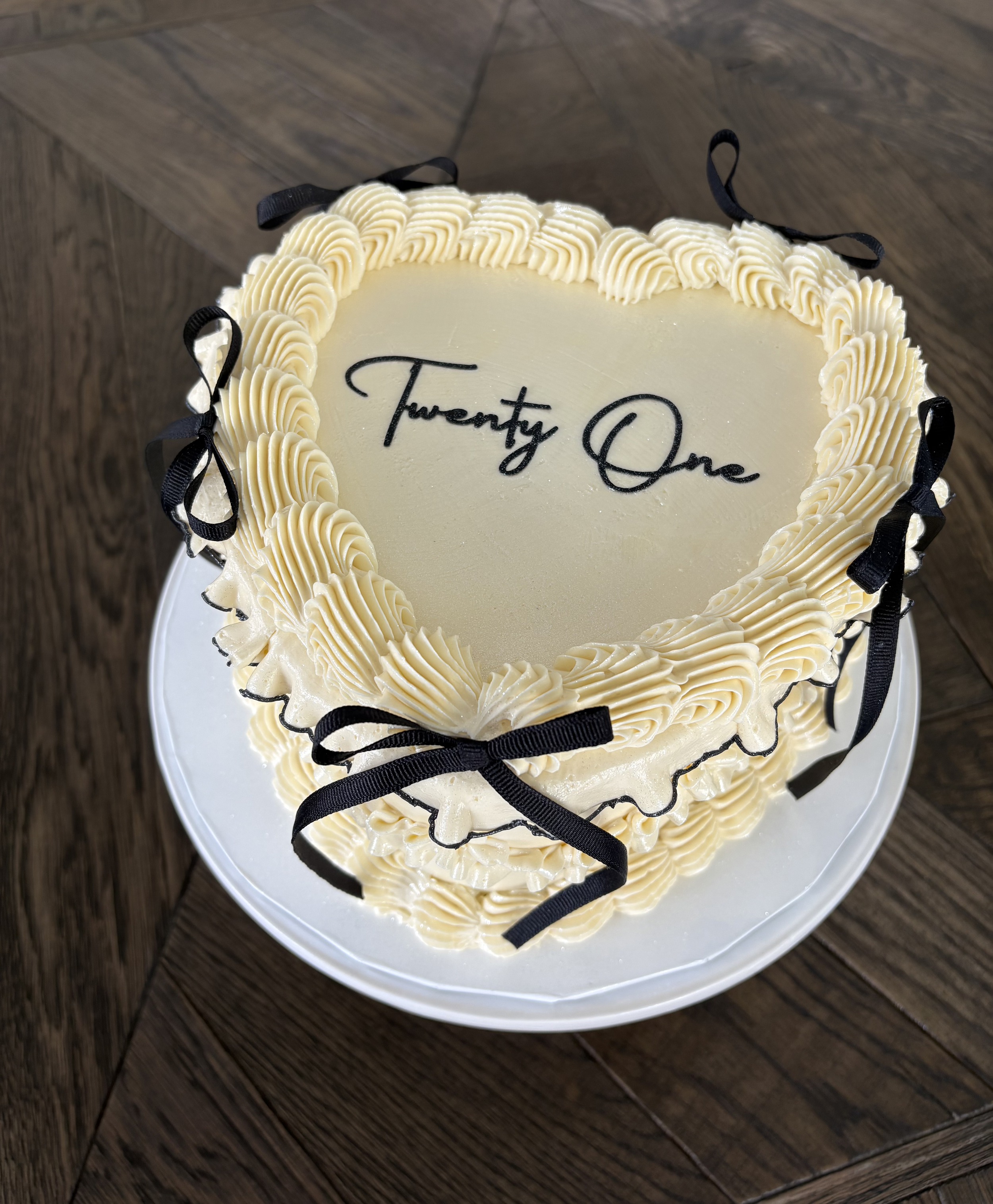 Heart-shaped cake with white frosting, black ribbons, and the word 'Thirteen' written in black on top.