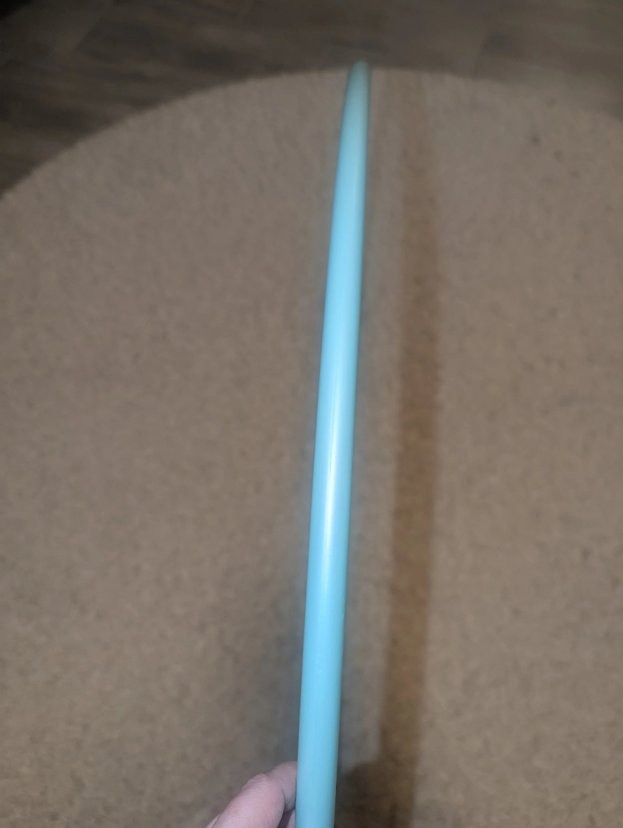 Ein blauer, runder Gegenstand mit seitlicher Ansicht, möglicherweise ein Hula-Hoop-Reifen, vor einem beigen Teppich.