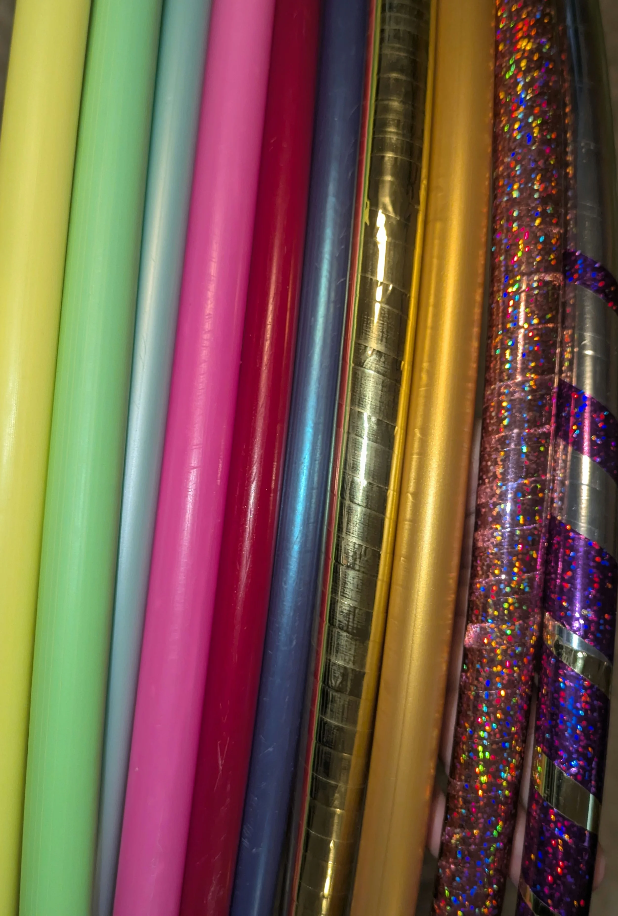 Mehrere bunte Hula-Hoop-Reifen in verschiedenen Farben und Mustern. Einige haben metallische und glitzernde Oberflächen.