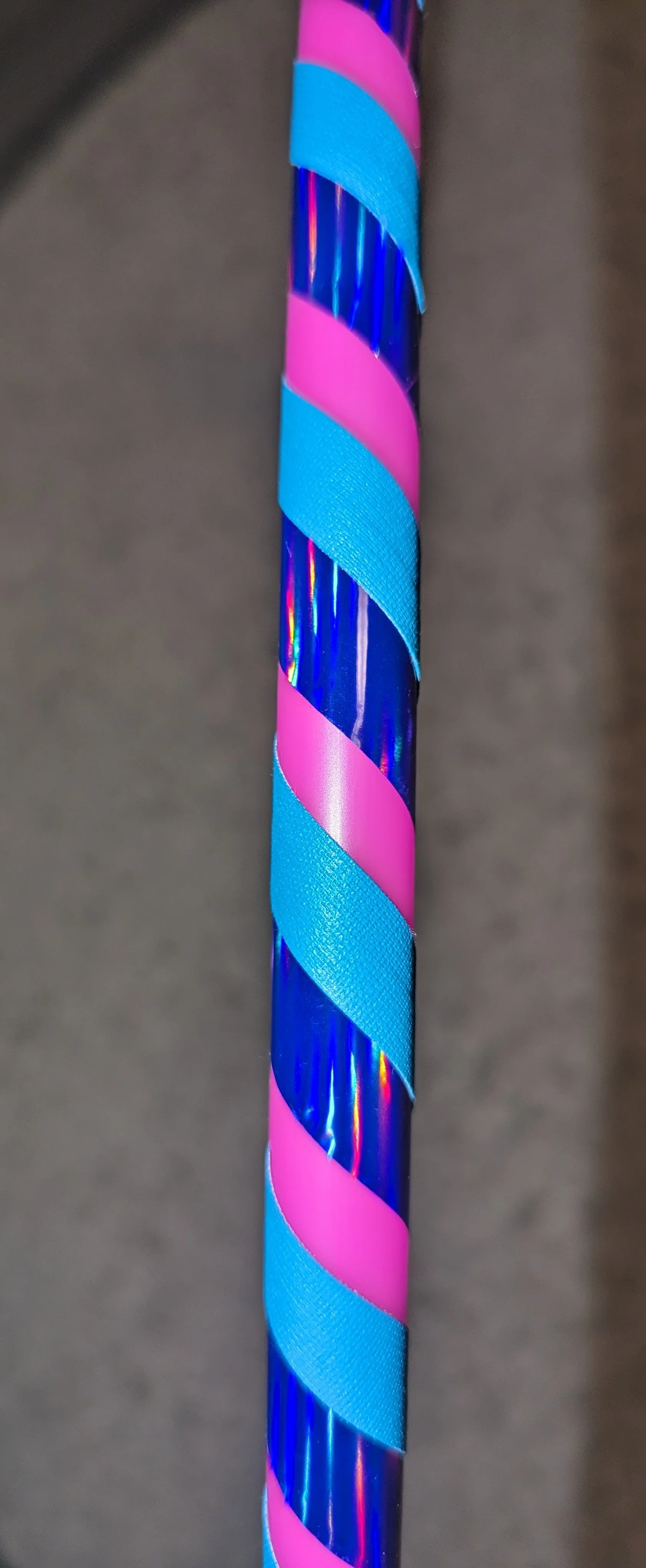 Nahaufnahme eines bunten Hula-Hoop-Reifens mit spiralförmigen Streifen in Blau, Pink und metallischem Glanz.