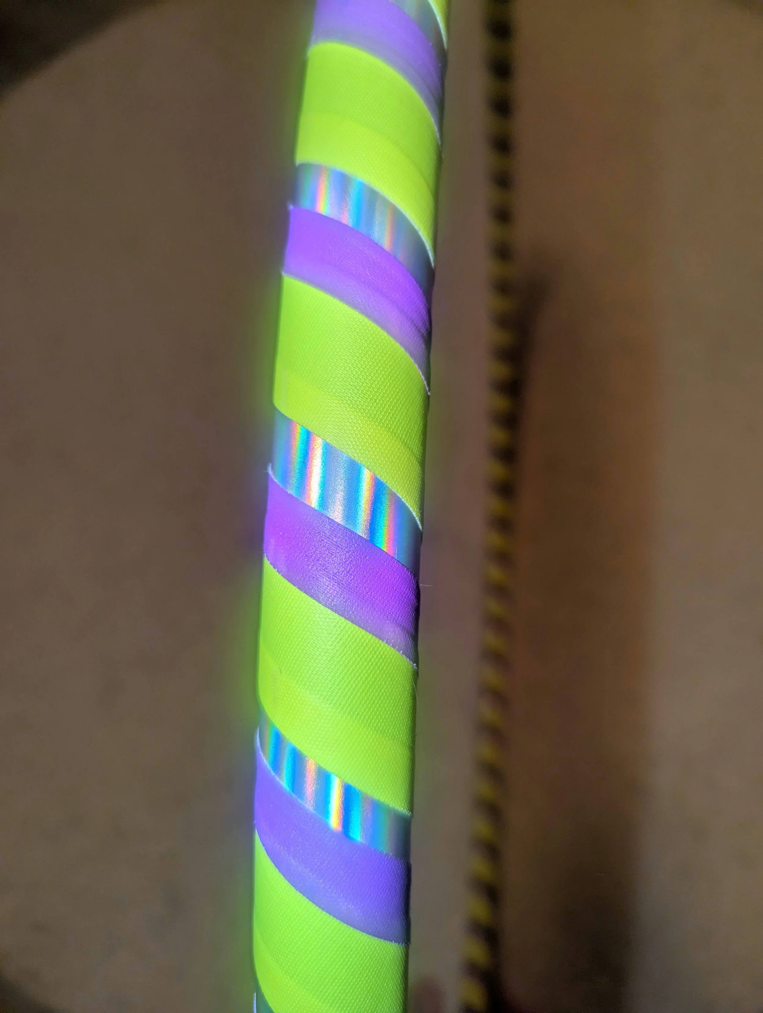 Nahaufnahme eines bunt gestreiften Hula-Hoop-Reifens mit leuchtenden grünen, lila und schillernden Streifen auf einem unscharfen Hintergrund.