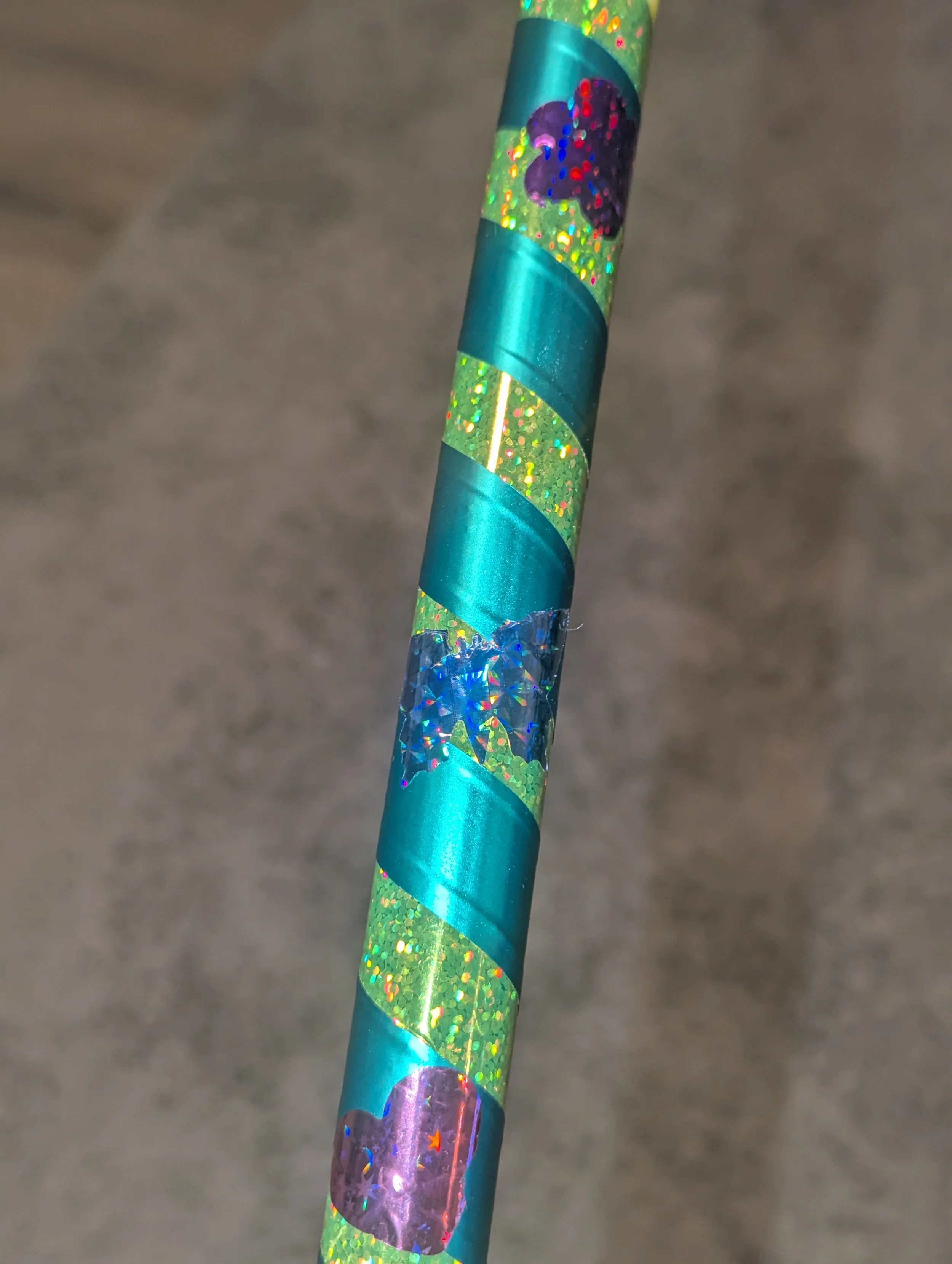 Nahaufnahme eines glitzernden, bunt verzierten Bleistifts mit holografischen Herzaufklebern und glänzendem, spiralförmigem Band auf einer unscharfen Oberfläche.