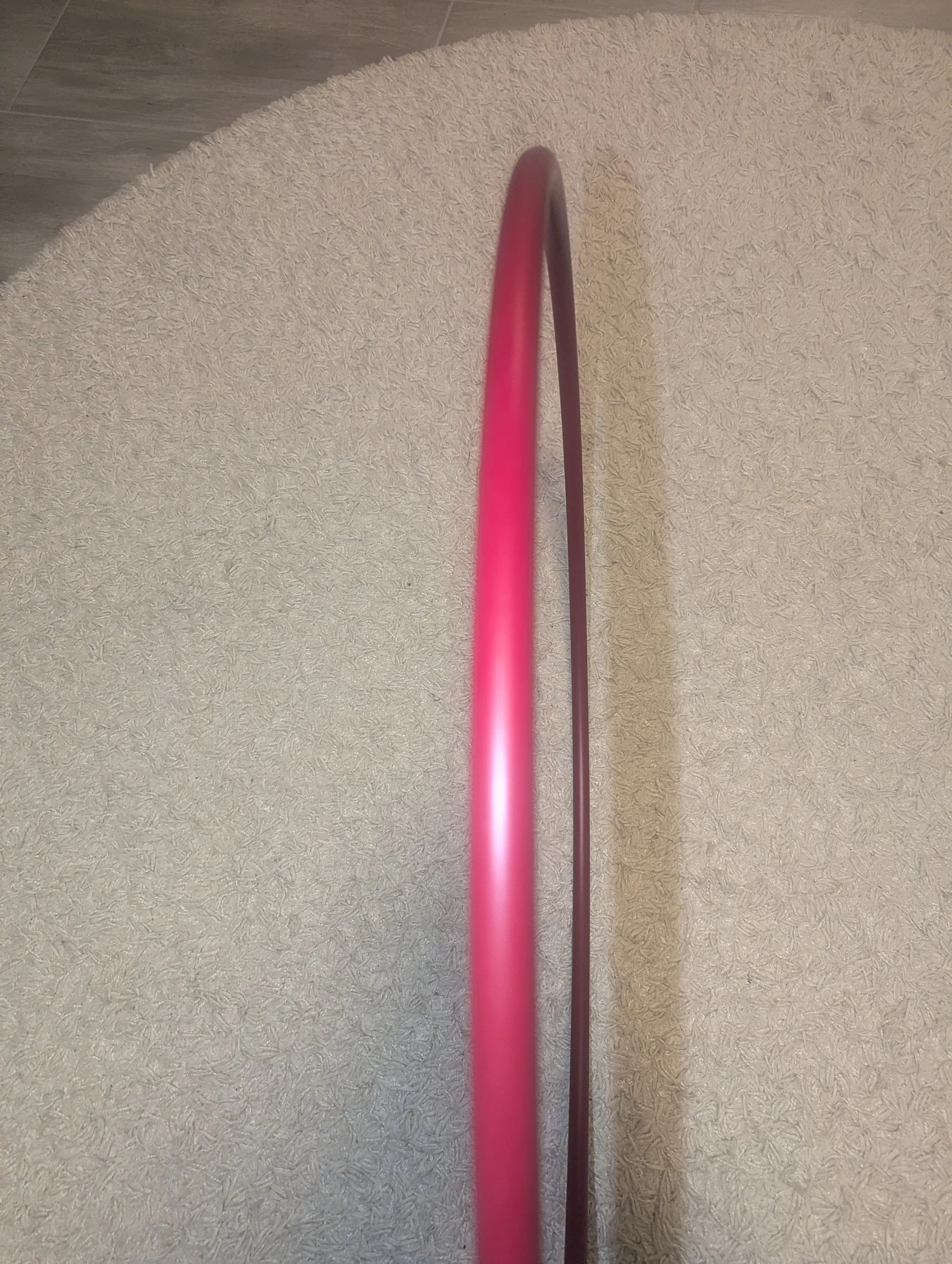 Ein roter Hula-Hoop-Reifen steht vertikal auf einem hellen Teppich.