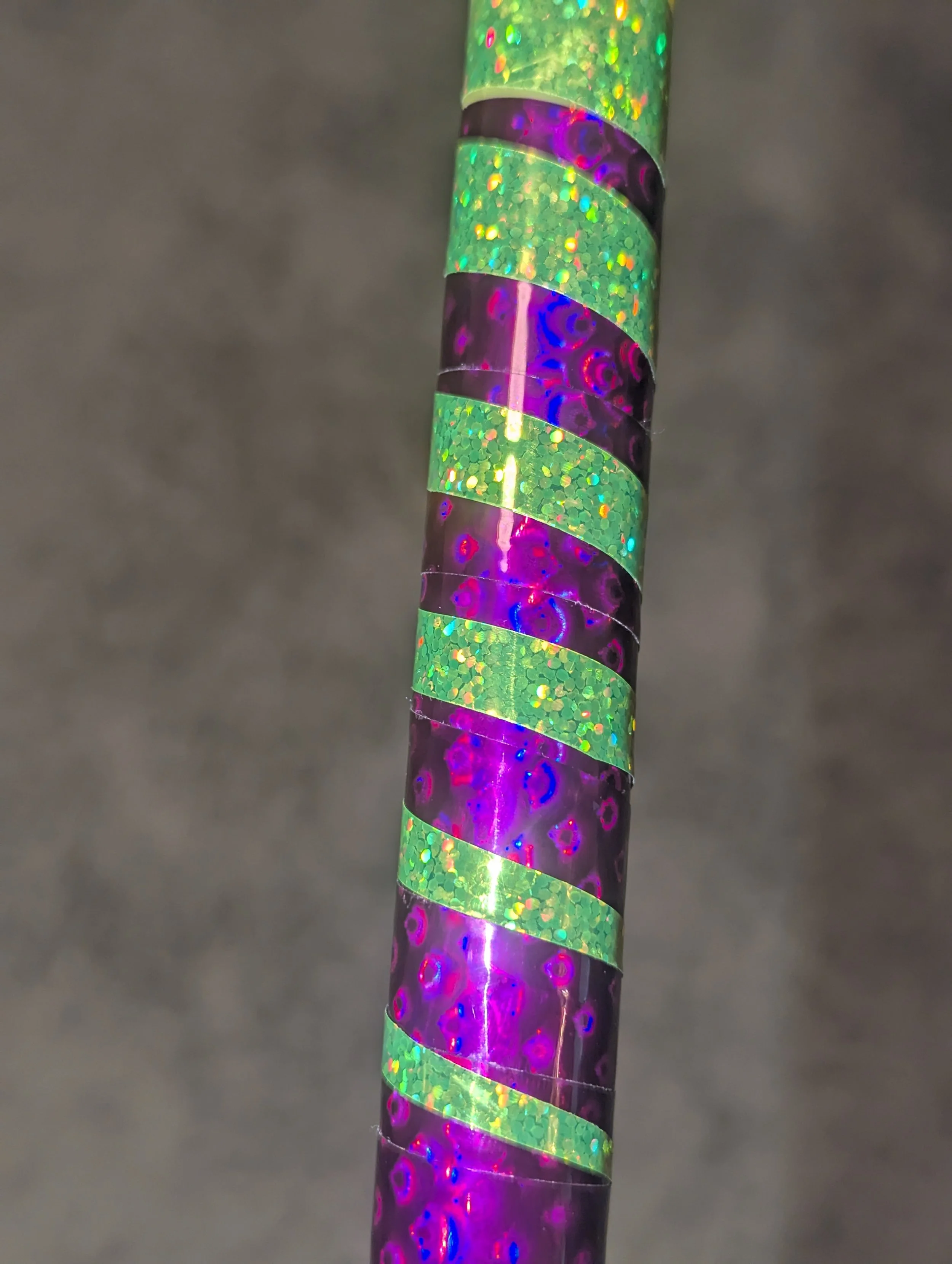 Ein Stab mit glänzenden, spiralförmigen Bändern in lila und grünem Glitzer.