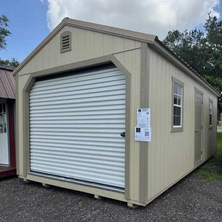 Yellow shed with a roll-up door and two windows, located outdoors with a gravel ground and trees in the background.