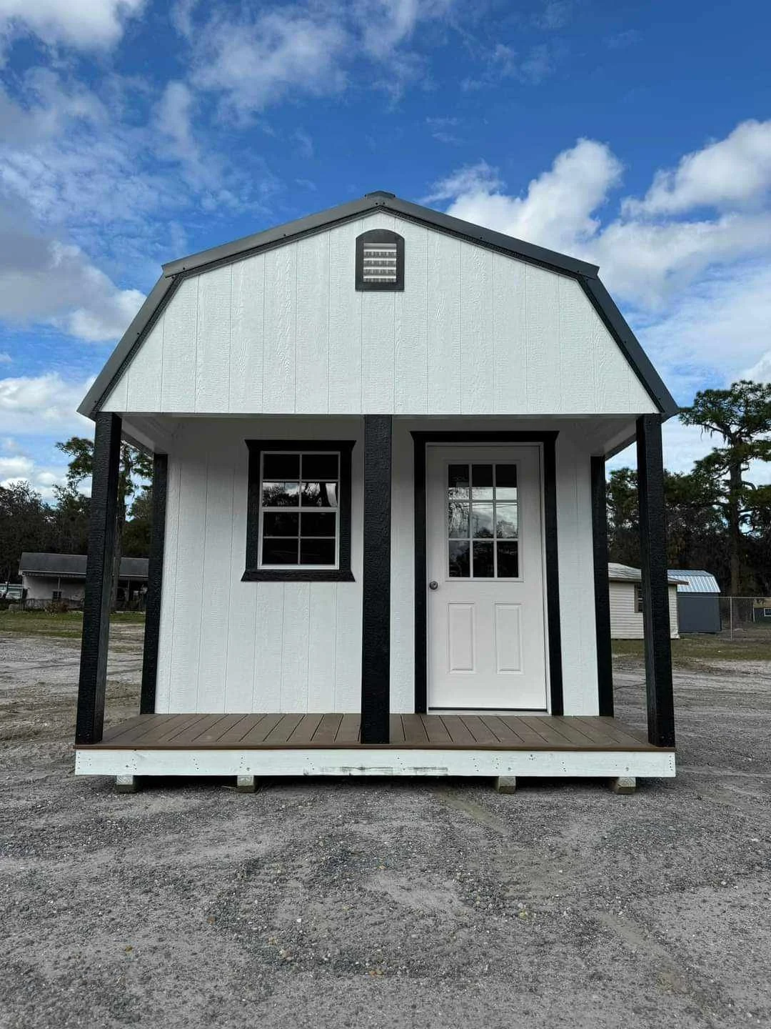 Small white lofted barn cabin shed with black trim and a porch, under a partly cloudy sky.