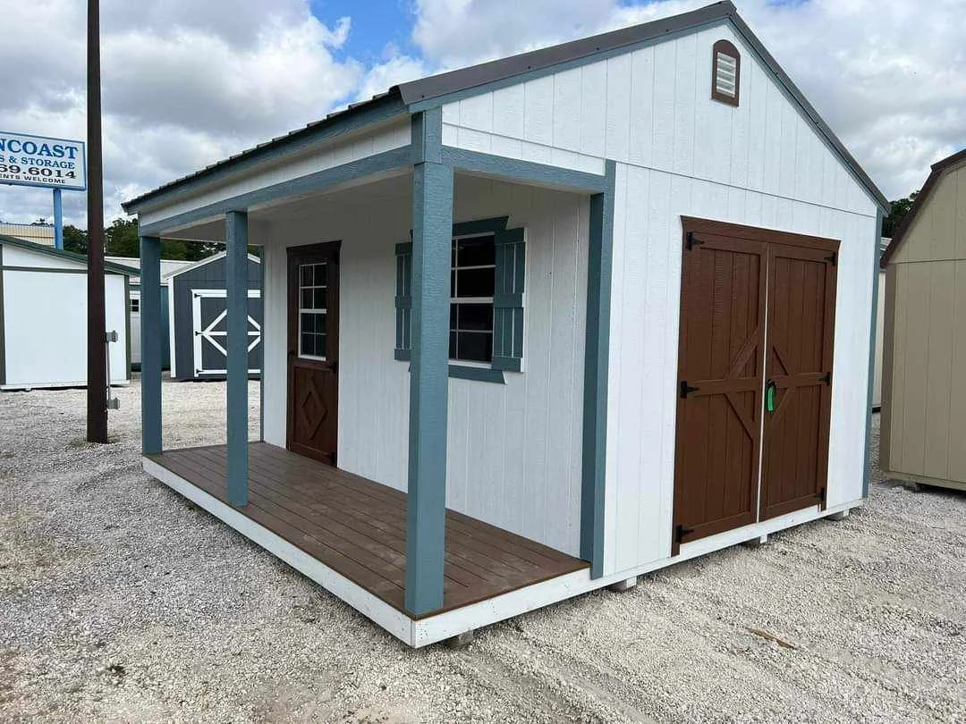A small shed with white walls, brown doors, and a small front porch with a wooden floor and blue porch posts.
