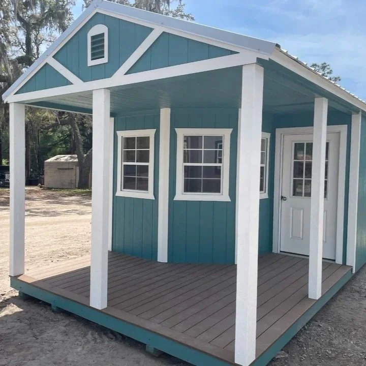Small blue playhouse with white trim and a porch, located outdoors on a dirt area.