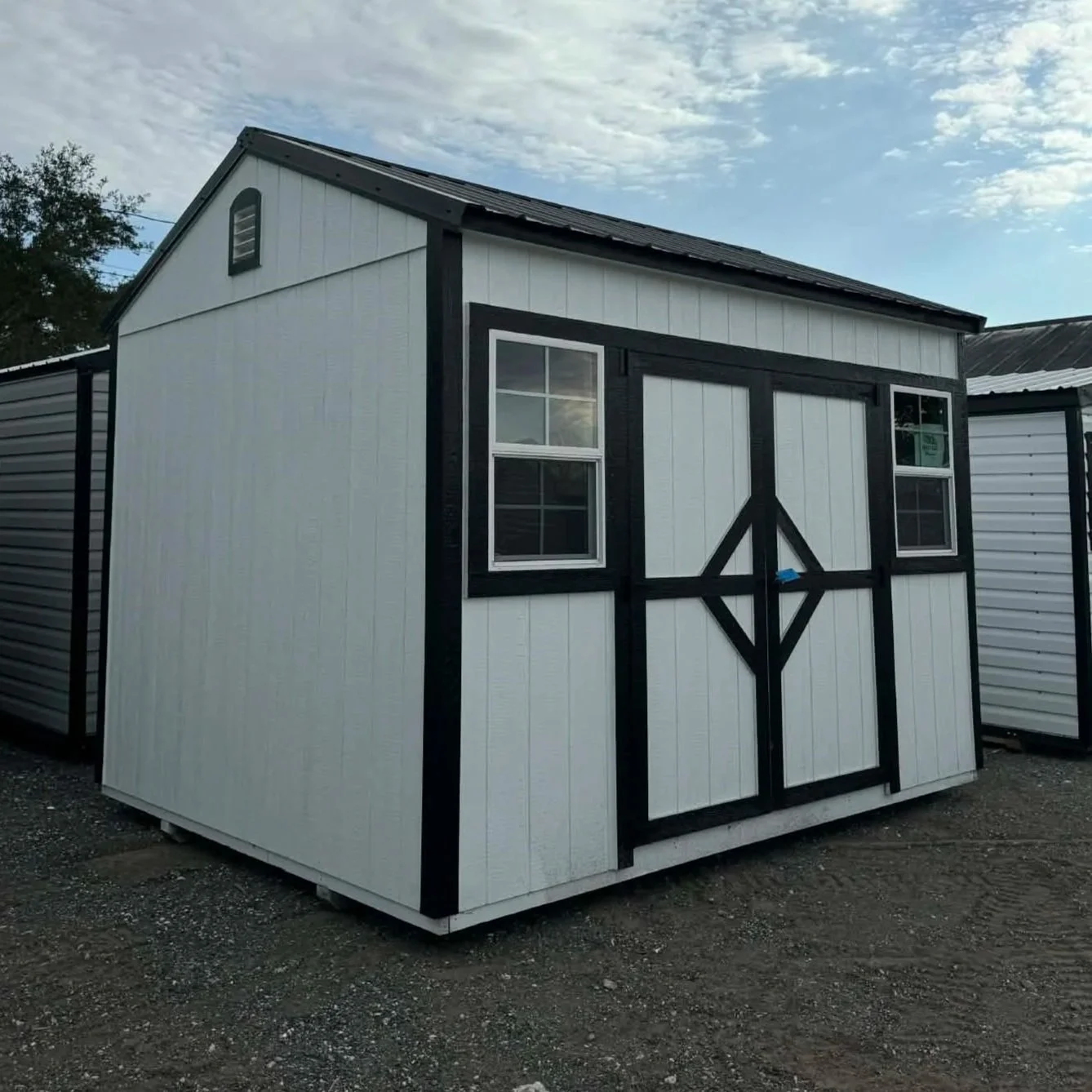 A small white shed with black trim and a black door with decorative black framing. It has two small windows with white frames.