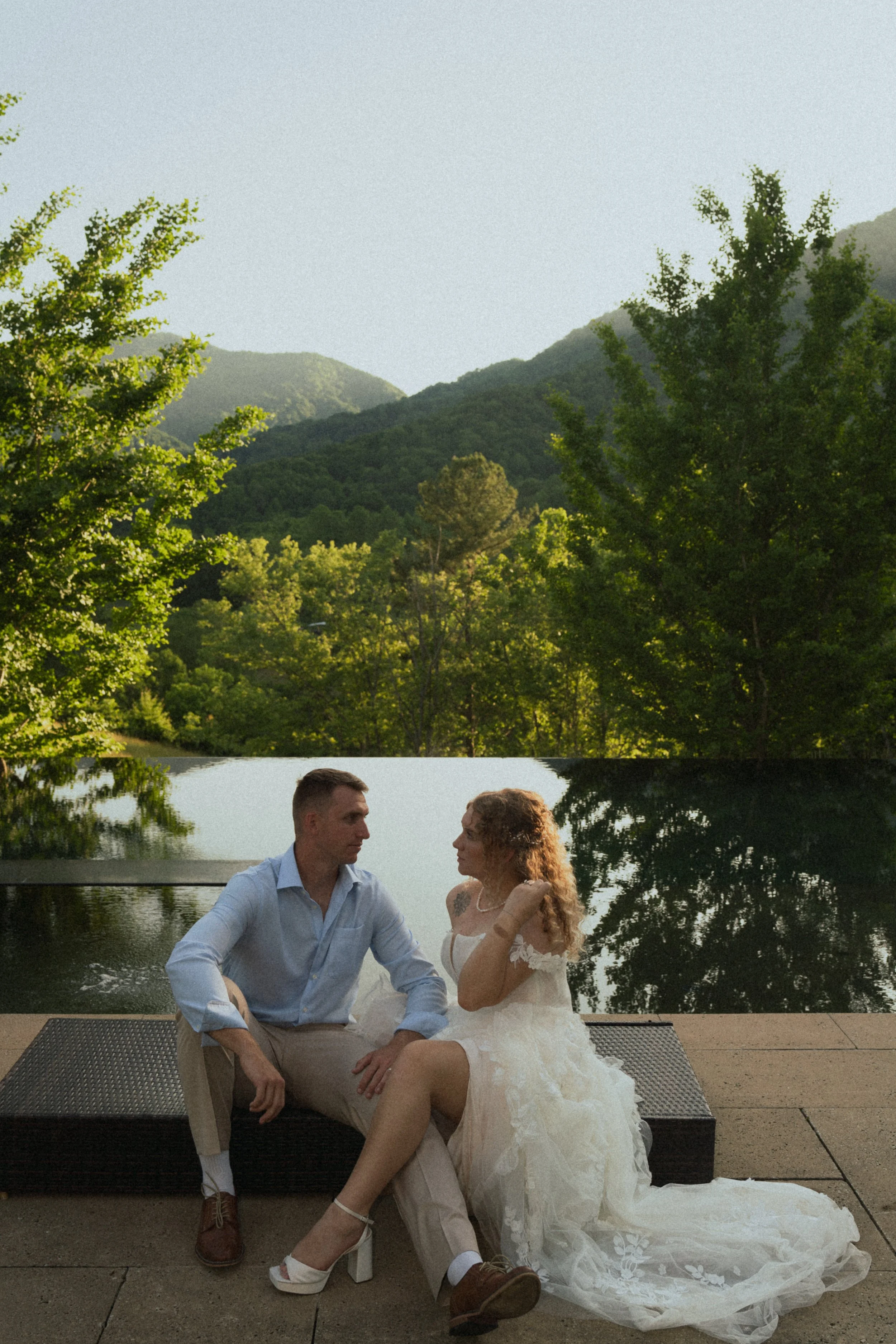 Editorial wedding portrait of bride in a tulle dress and groom in slacks and dress shirt sitting in the middle of the Blue Ridge Mountains in Leicester during golden hour