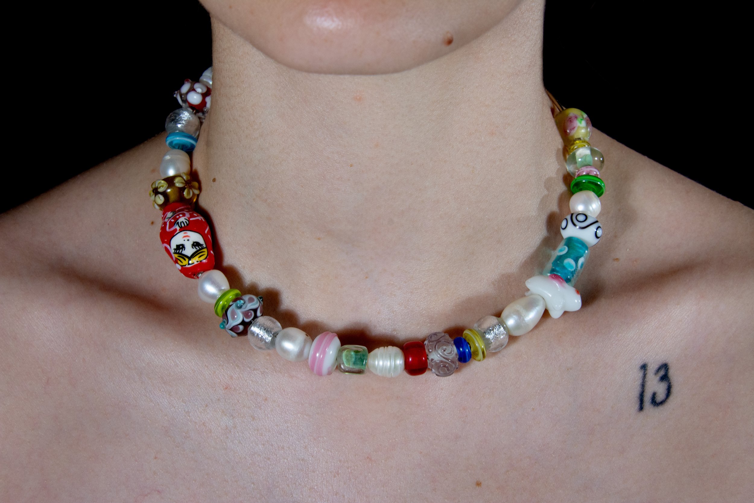 Model's neck and chest area pictured wearing Steel wire choker necklace with varied multicolor and pearl beads on black background