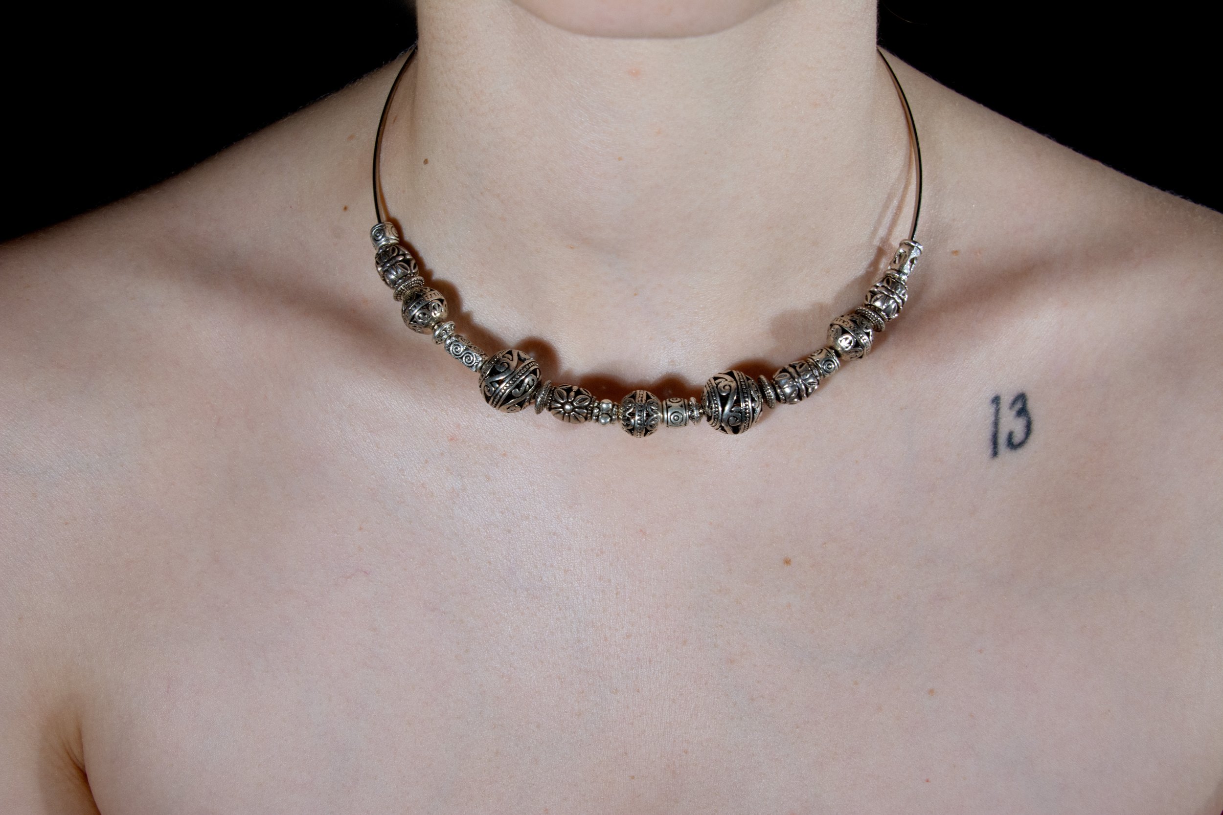 Model's neck and chest area pictured wearing steel wire circular choker necklace with ornate silver charms against black background