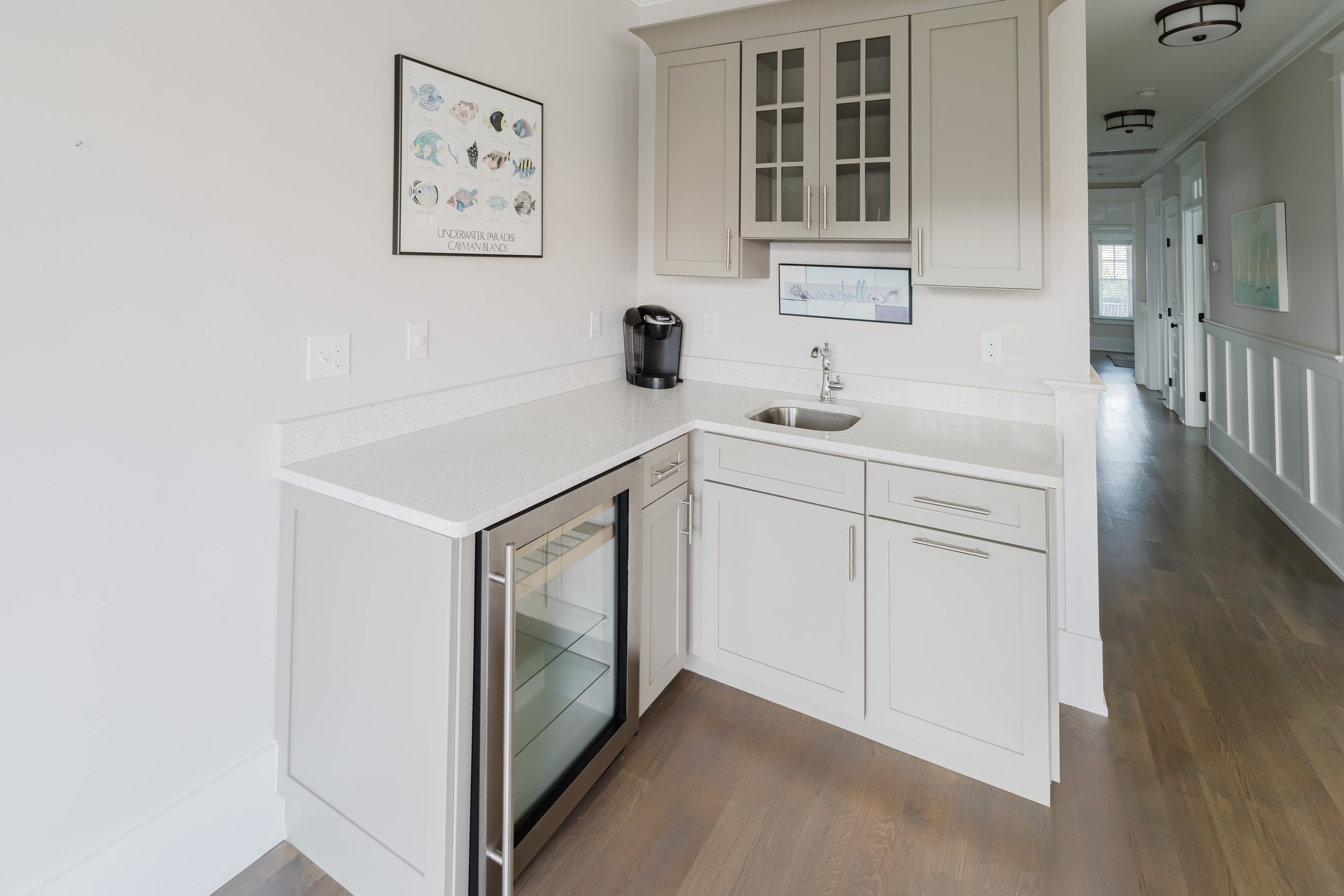 Home bar area with white cabinets, a countertop with a sink, a mini fridge, and a coffee maker.