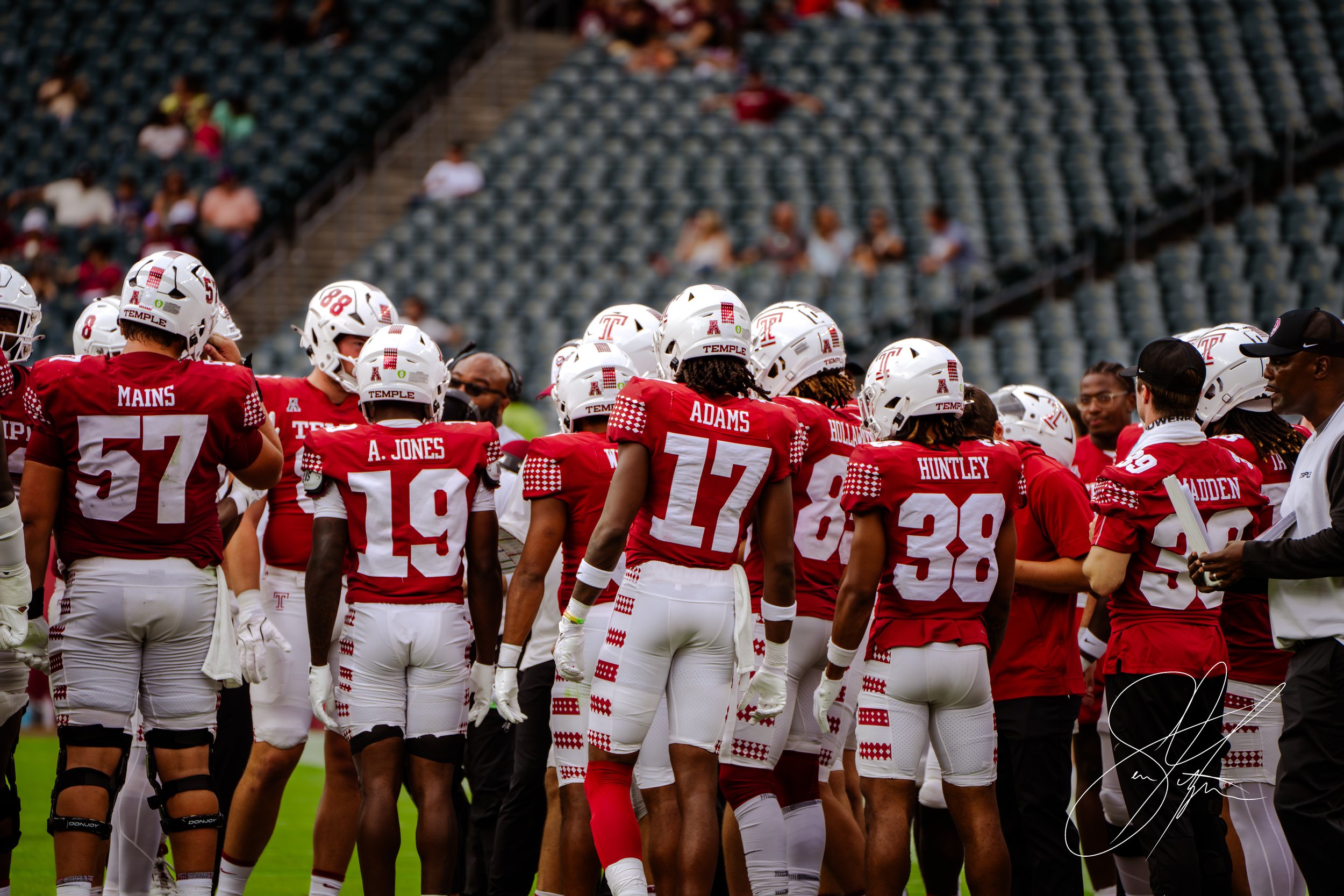 Group of American football players in red and white uniforms huddled on a field.
