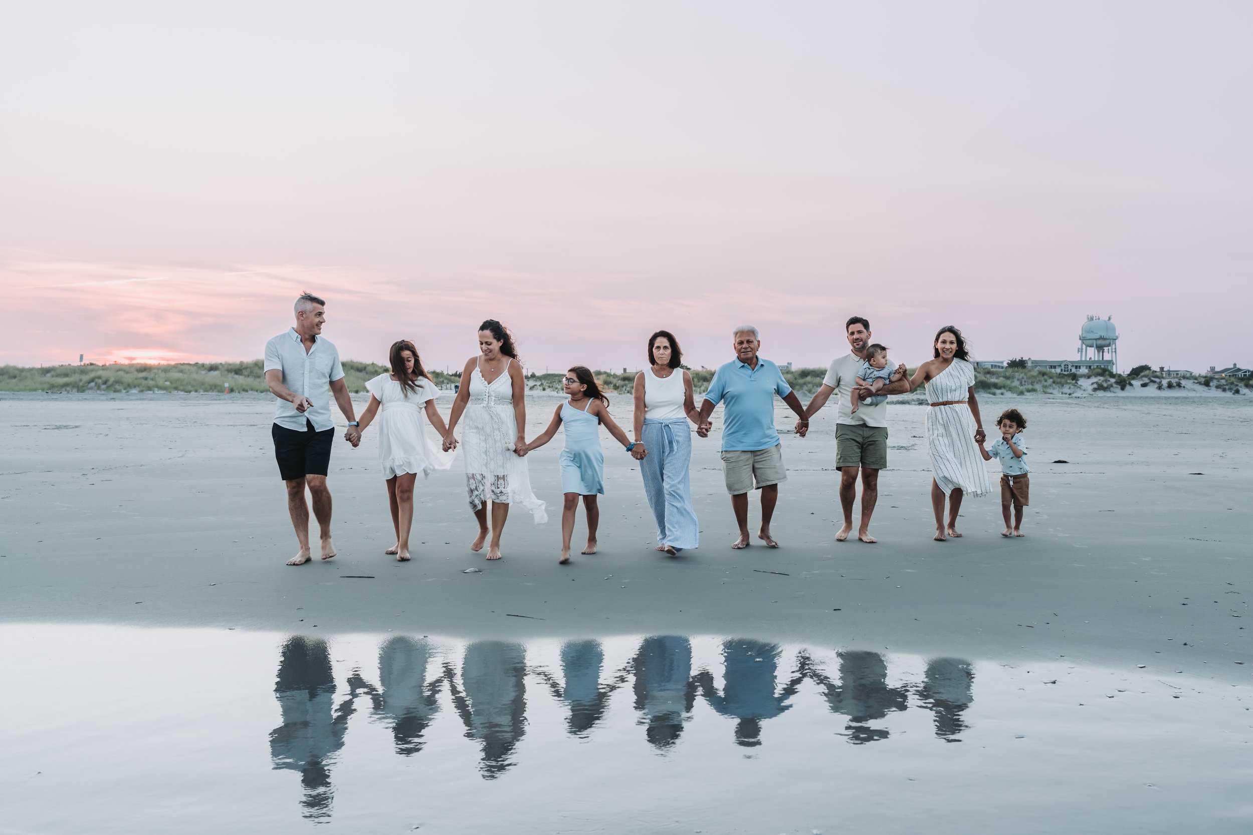 Family walking hand-in-hand on a beach at sunset, reflecting in the wet sand.