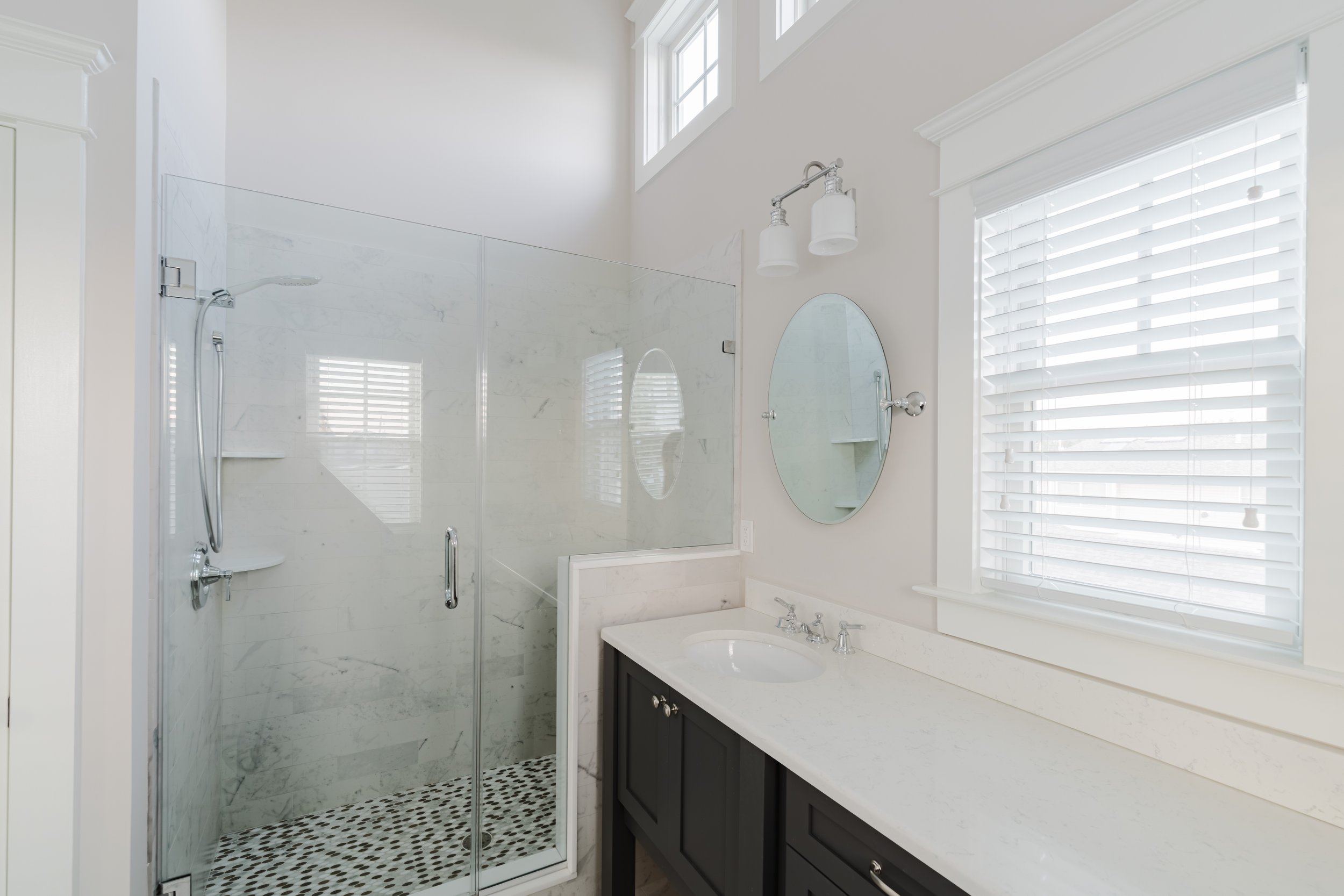 Modern bathroom with glass shower, white countertop, sink, and oval mirror.