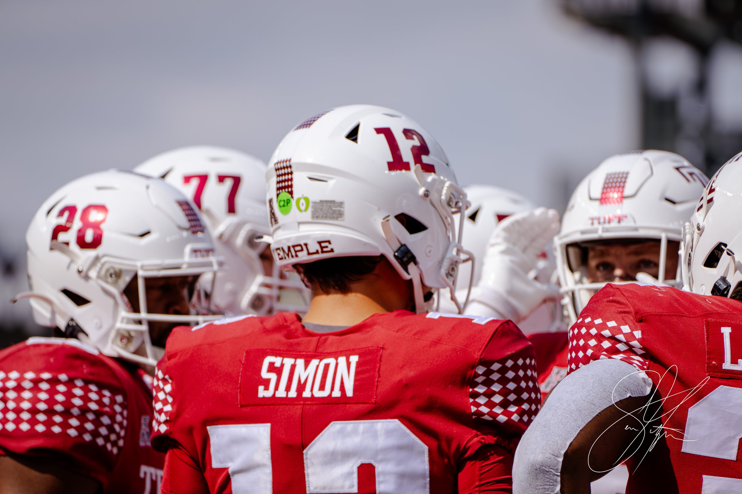 Football players in red uniforms and white helmets huddling on the field, with "Temple" and "Simon" visible on jerseys.
