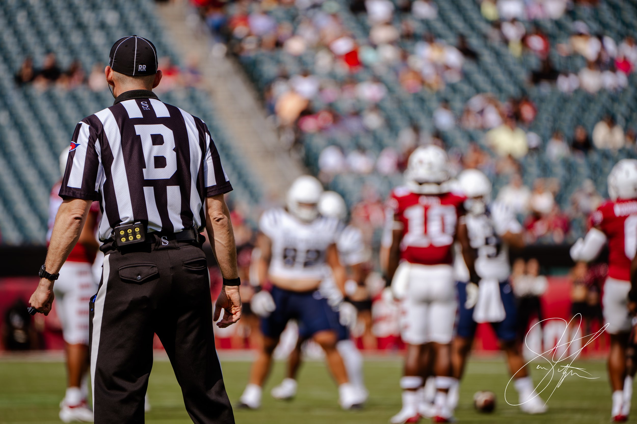 Football referee on field with players in background during a game.
