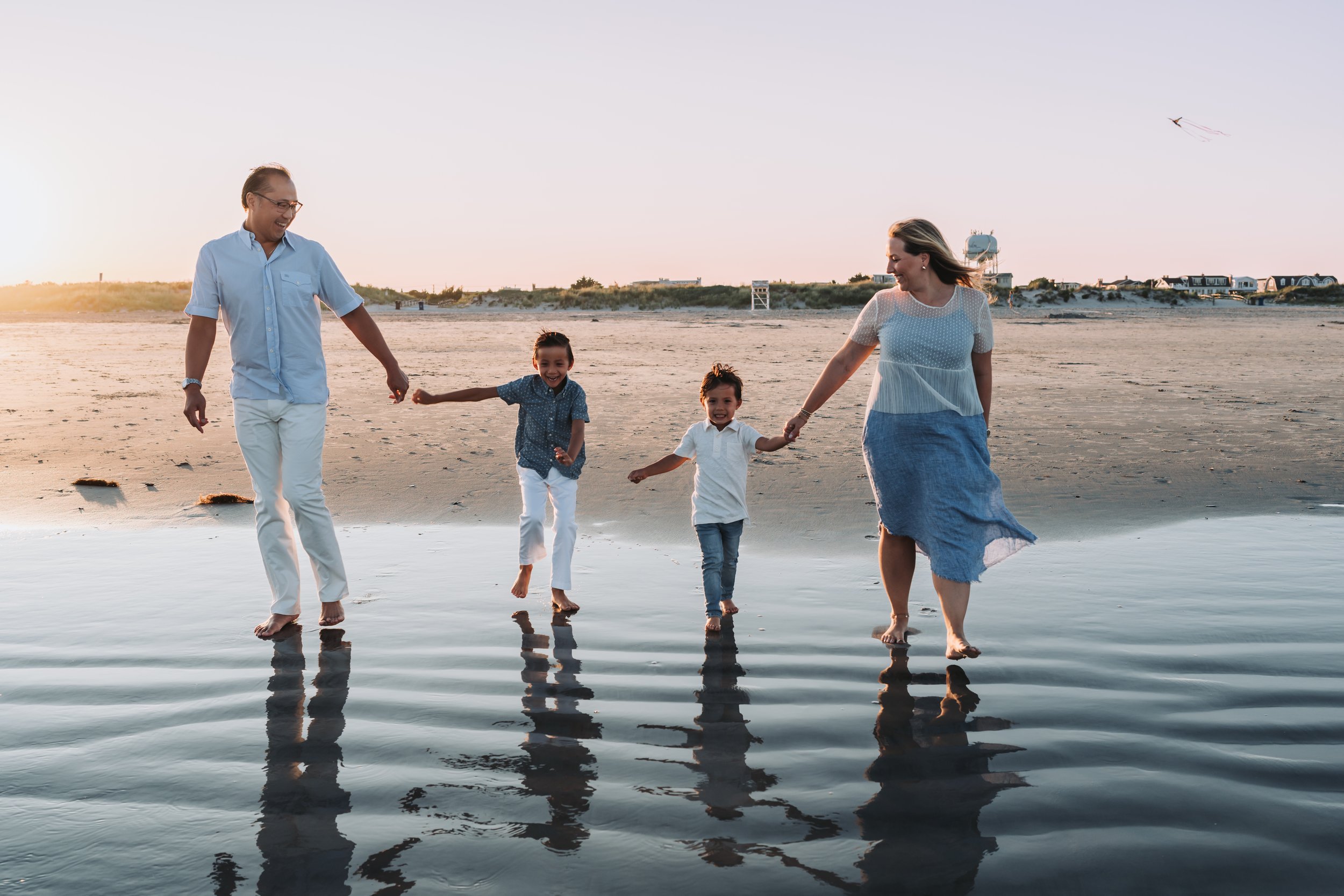 Family walking on beach shoreline at sunset, holding hands and smiling.