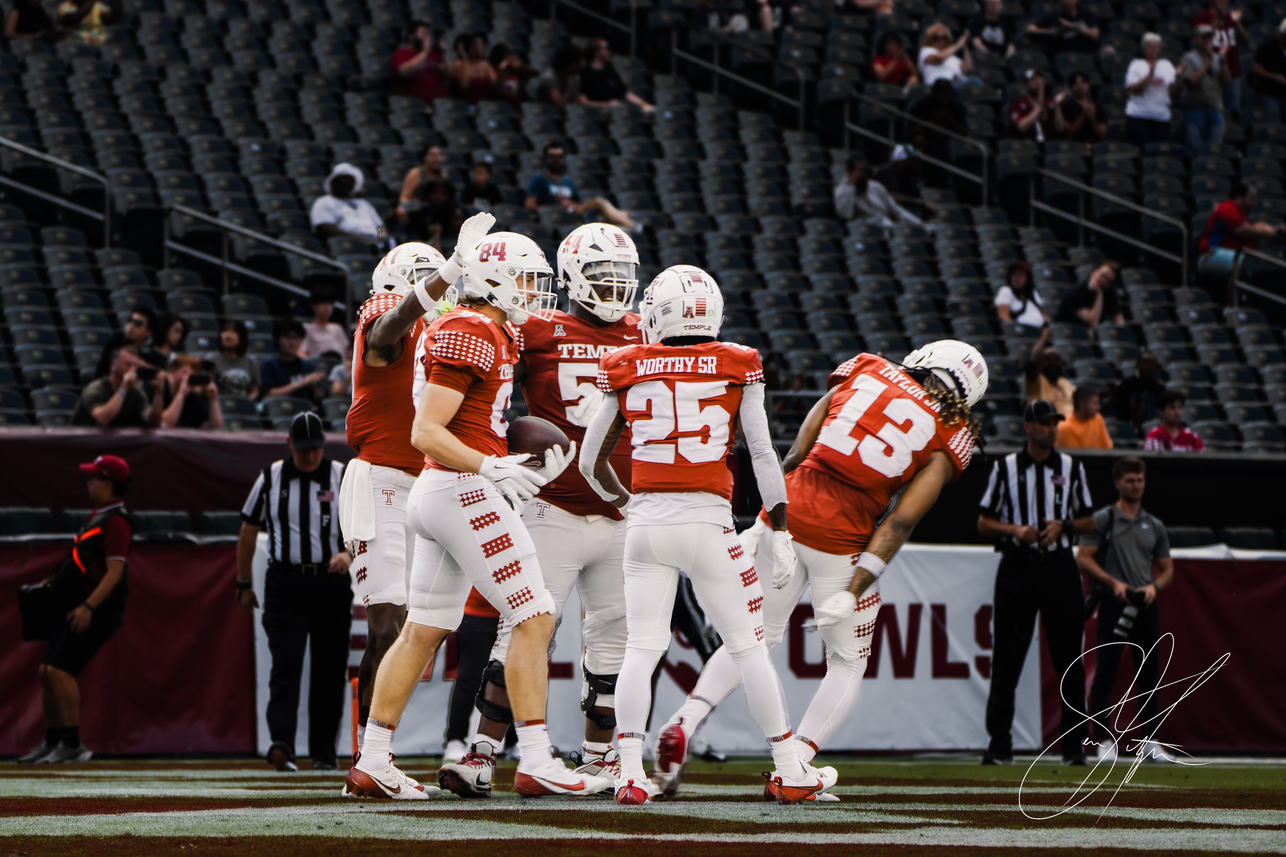 College football players in red uniforms celebrating on the field during a game, with referees and spectators in the background.