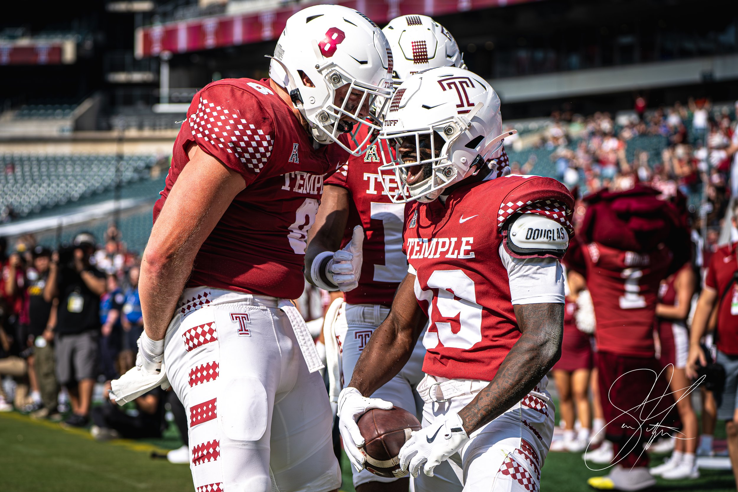 Temple University football players in red and white uniforms celebrate on the field during a game.