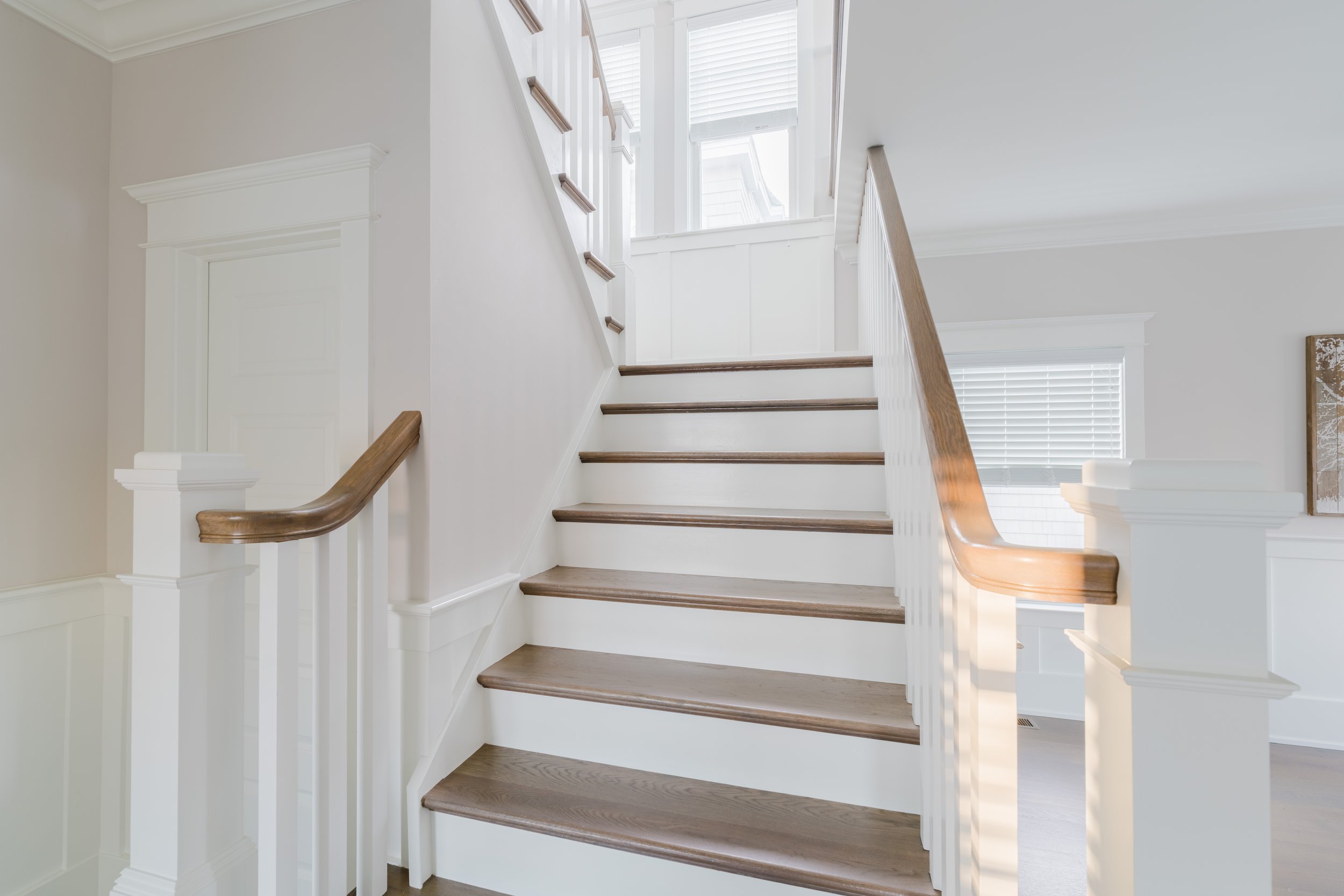 Interior staircase with wooden steps and white balusters, leading to an upper floor with windows.