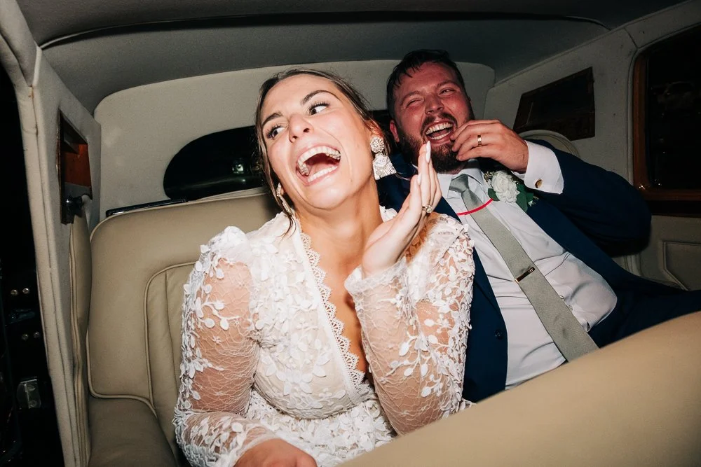 A couple laughs together in their get away car after their fun filled wedding