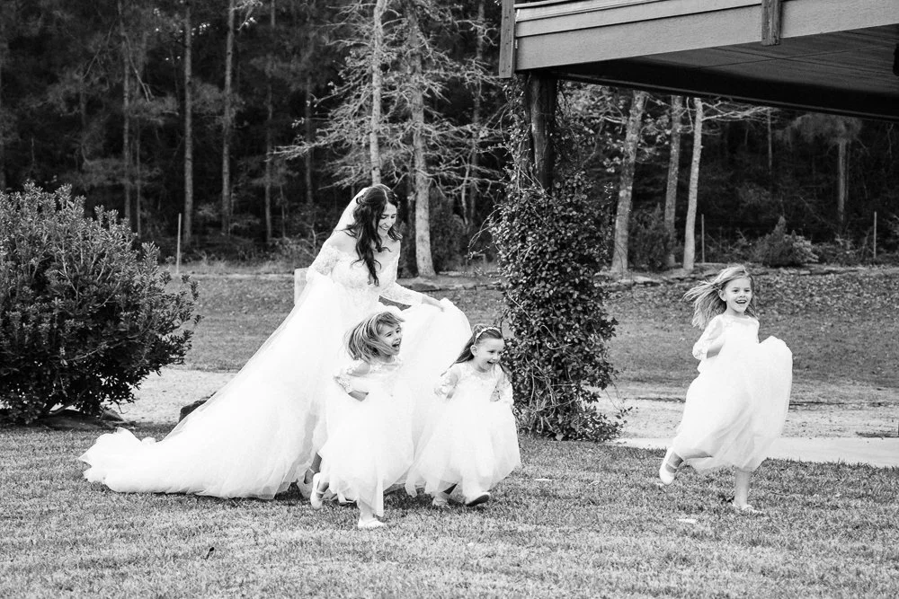 A bride runs across a lawn with three giggling flower girls