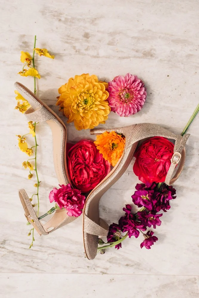 West Michigan wedding photo of bridal details. A pair of bridal heels are surrounded with pink, orange, yellow, and purple flowers.