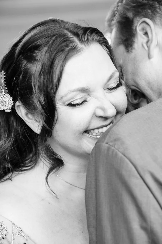 A couple embraces on their wedding day. The bride's face is visible behind the groom's shoulder grinning ear to ear. Photo by West Michigan wedding photographer libby dollar