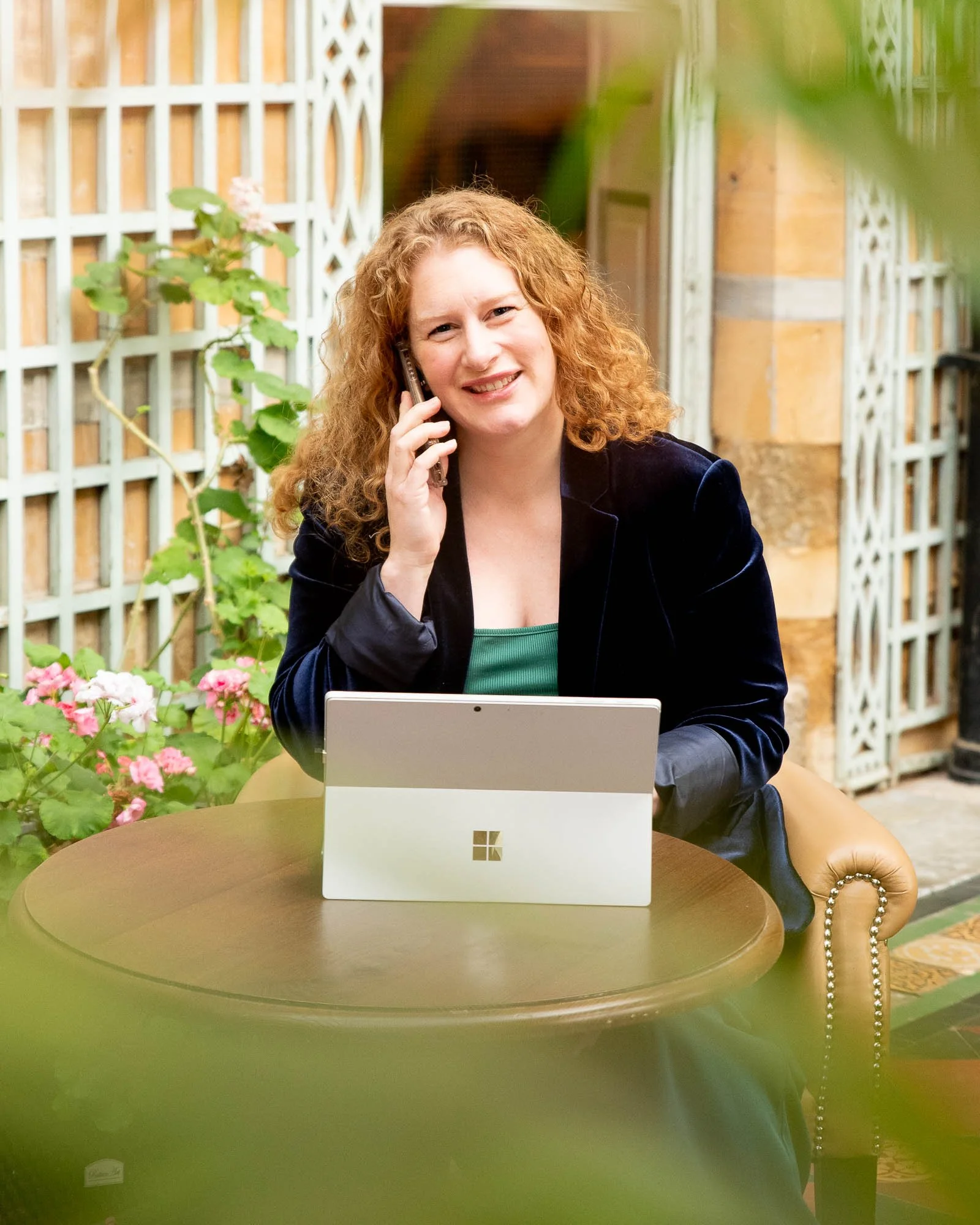 katie sitting at a laptop whilst on the phone looking at the camera smiling