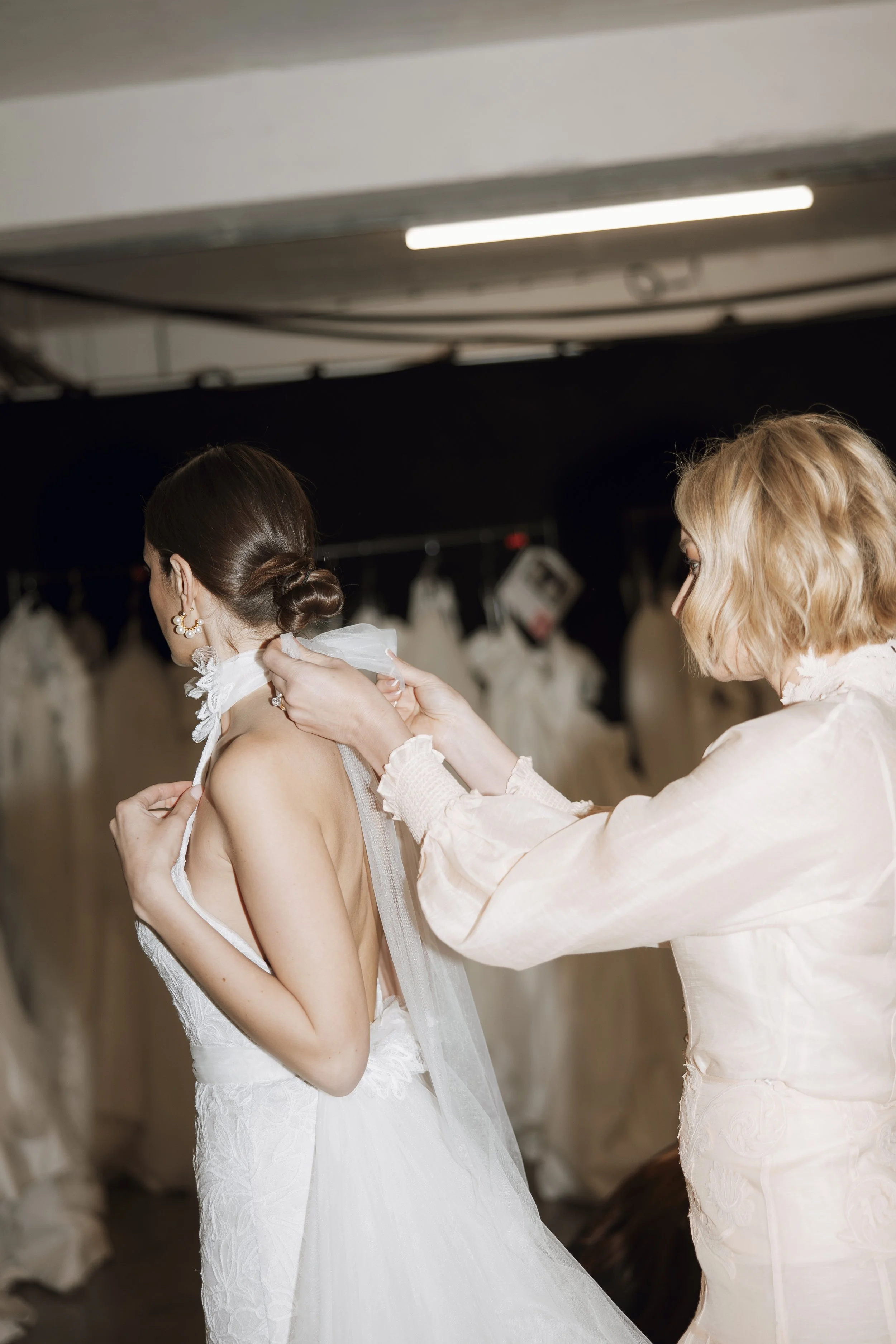  Behind the scenes at bridal fashion week London showing a designer surrounded by wedding gowns 