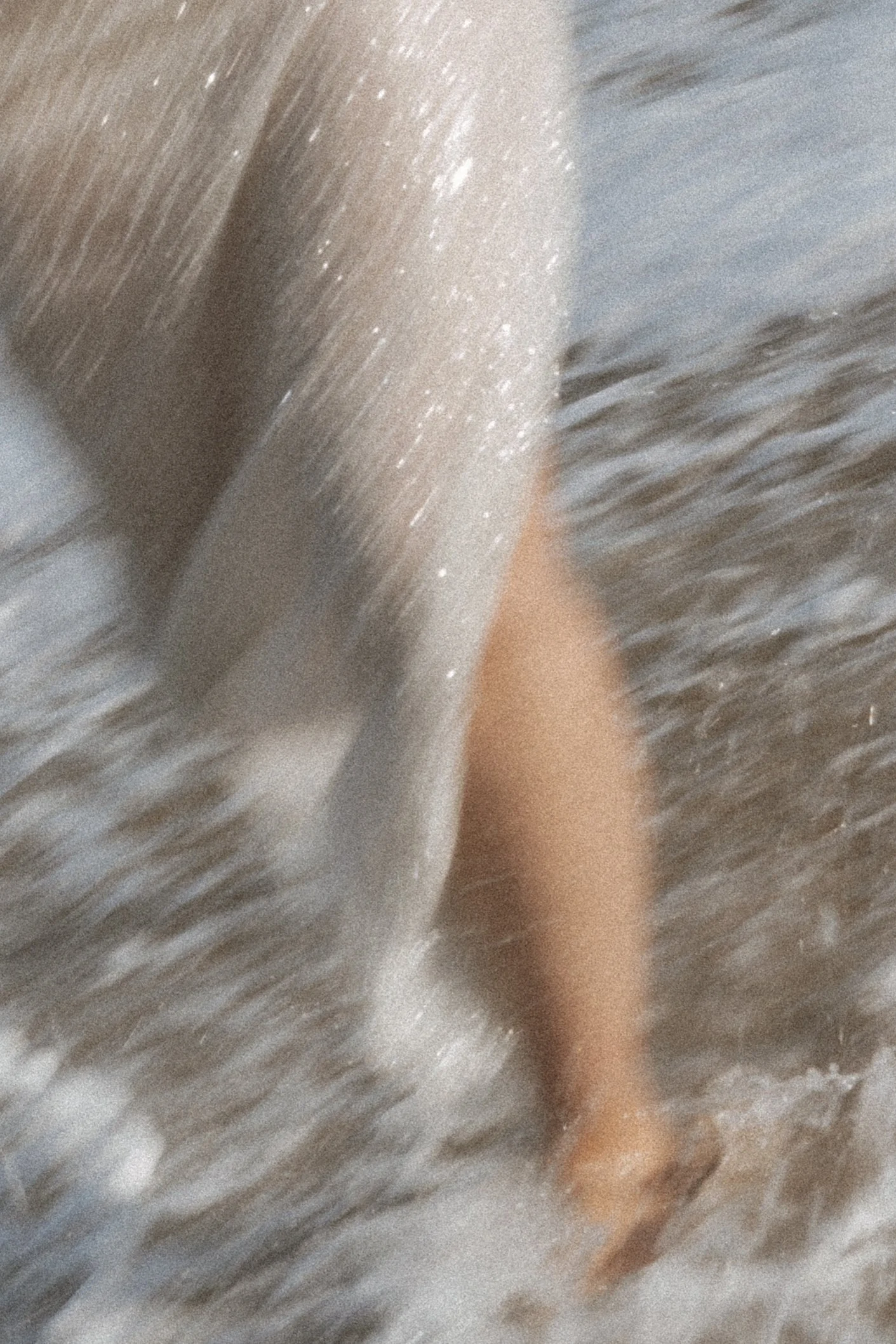 Abstract close-up of bride’s legs in the ocean with water movement and soft blur, editorial pre-wedding detail shot in Biarritz