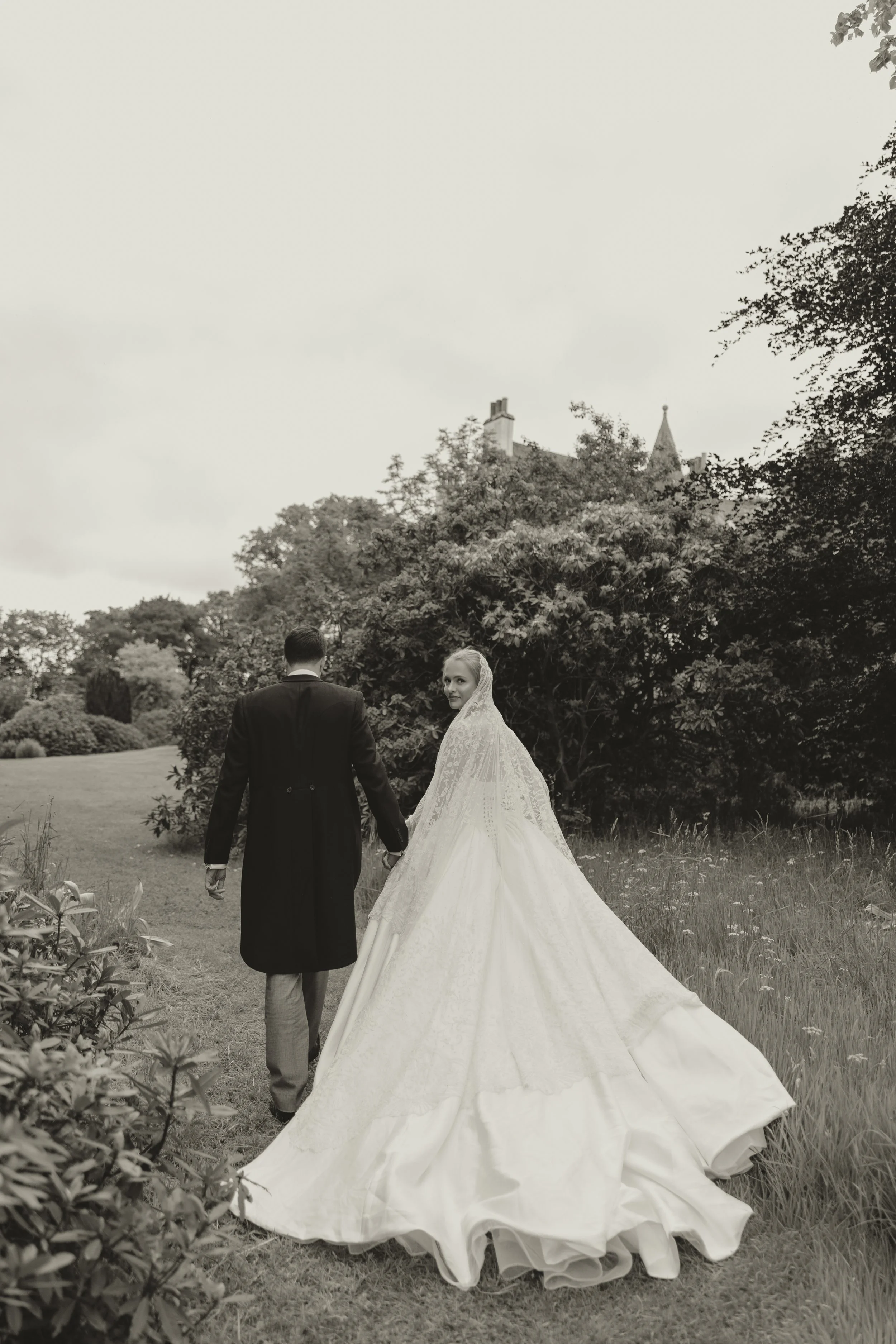 Luxury garden wedding portrait of a bride and groom walking through the grounds of a UK country house venue, photographed in black and white