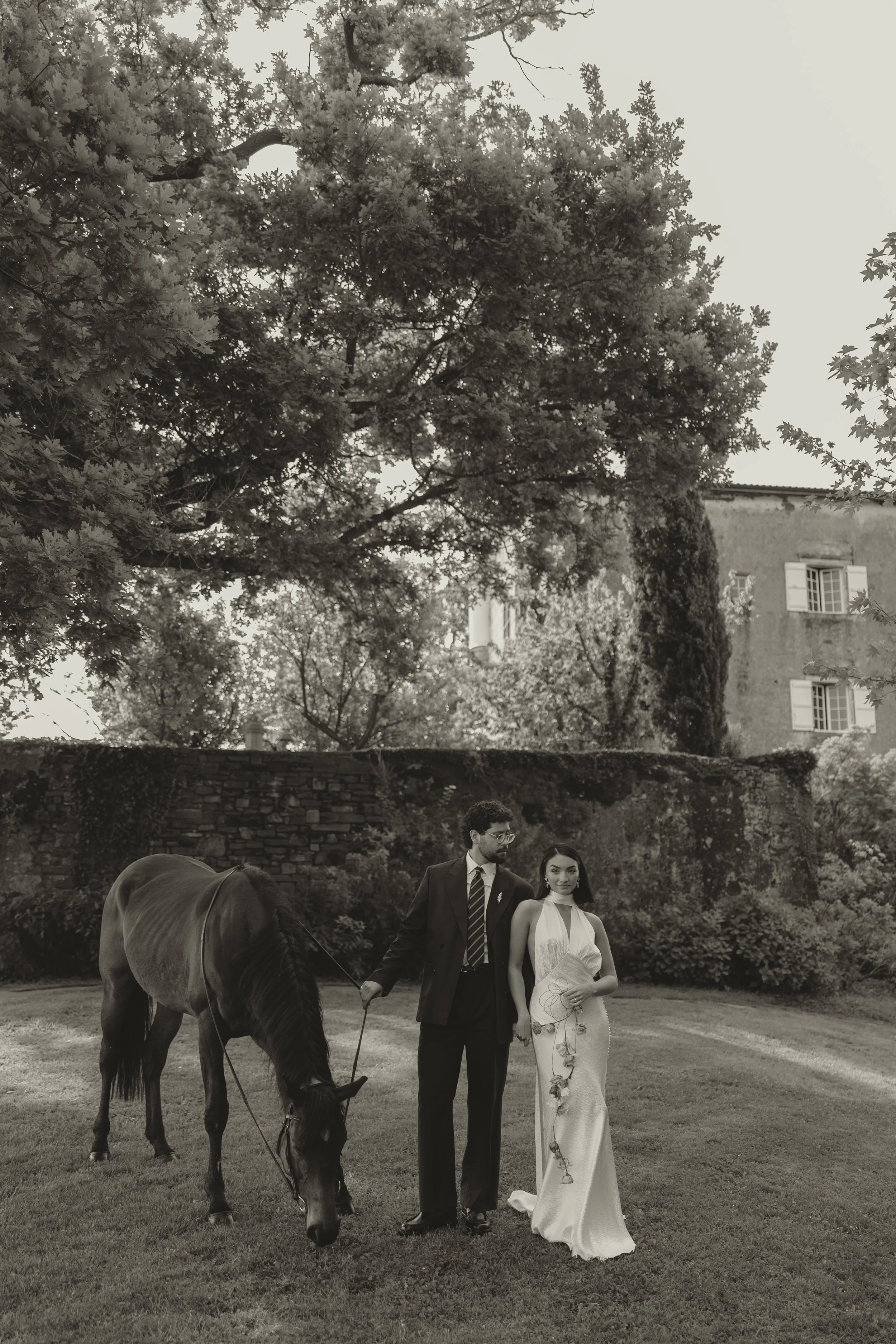 Luxury wedding photograph of a bride and groom standing with a horse at a french chateau, capturing a refined, fashion-inspired destination wedding moment