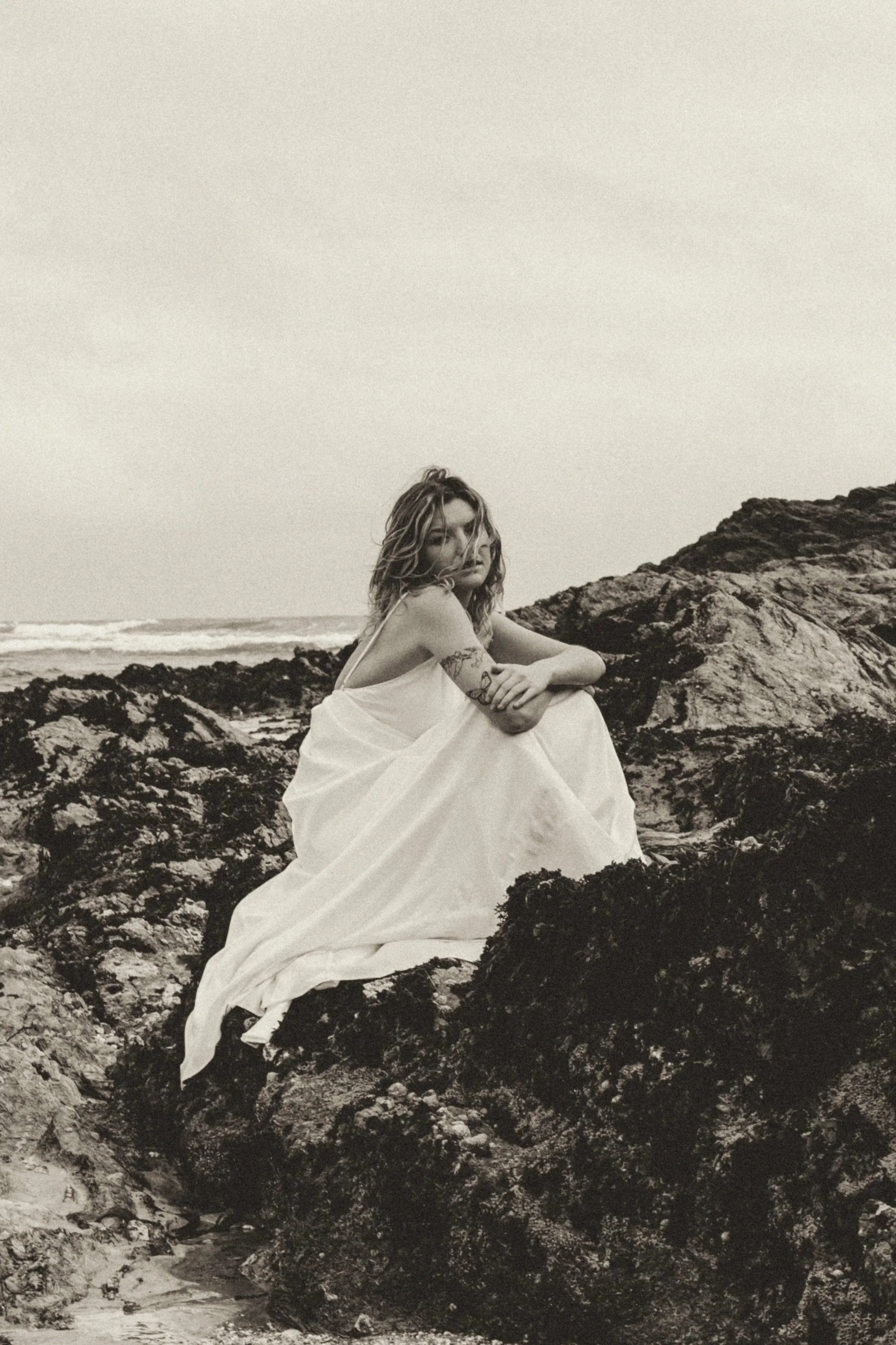 Bridal editorial at Maenporth Beach in Cornwall featuring a modern bride in a coastal, windswept setting