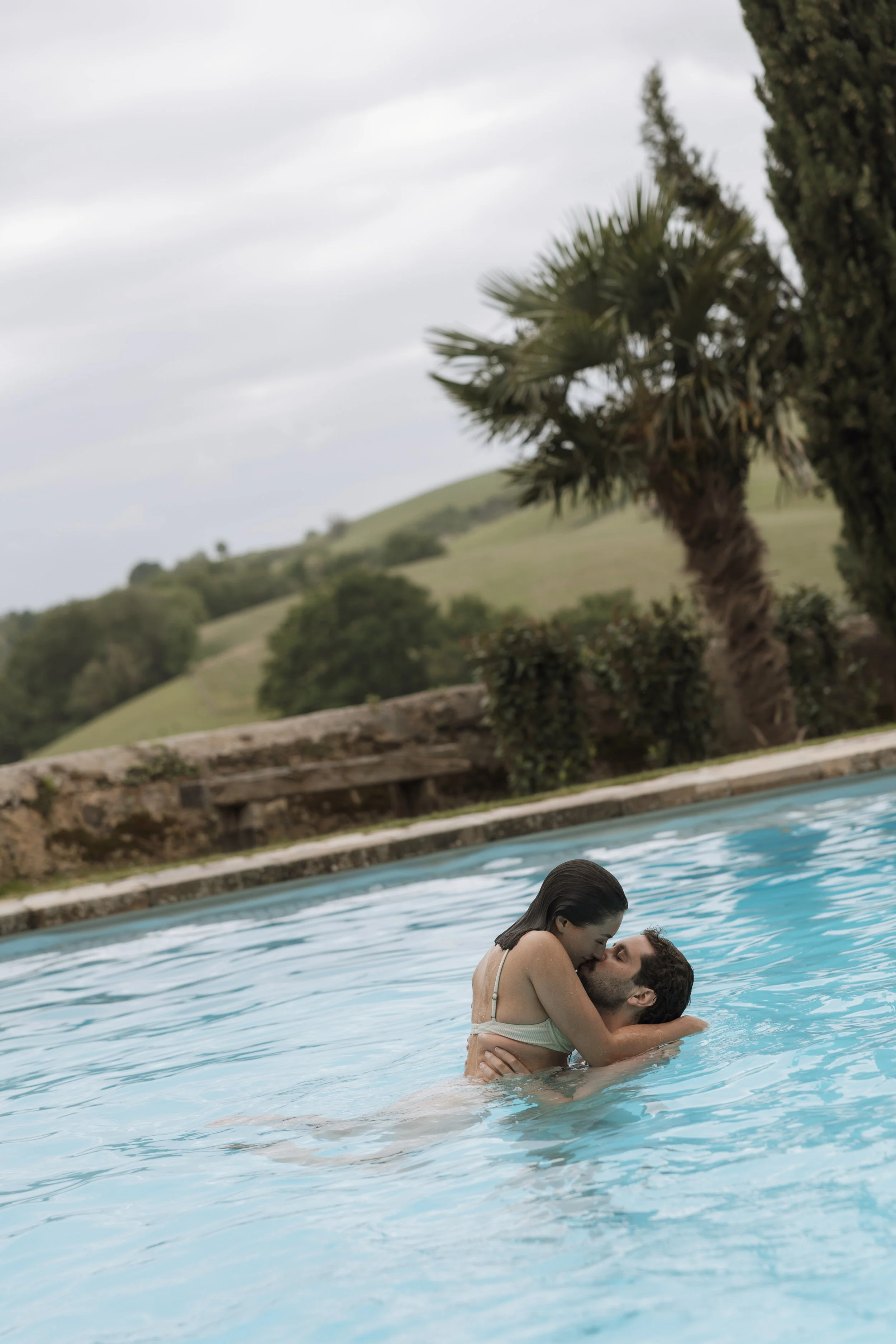 Editorial wedding photograph of a couple embracing in a pool, capturing a romantic, intimate destination wedding moment in a relaxed, fashion-inspired style