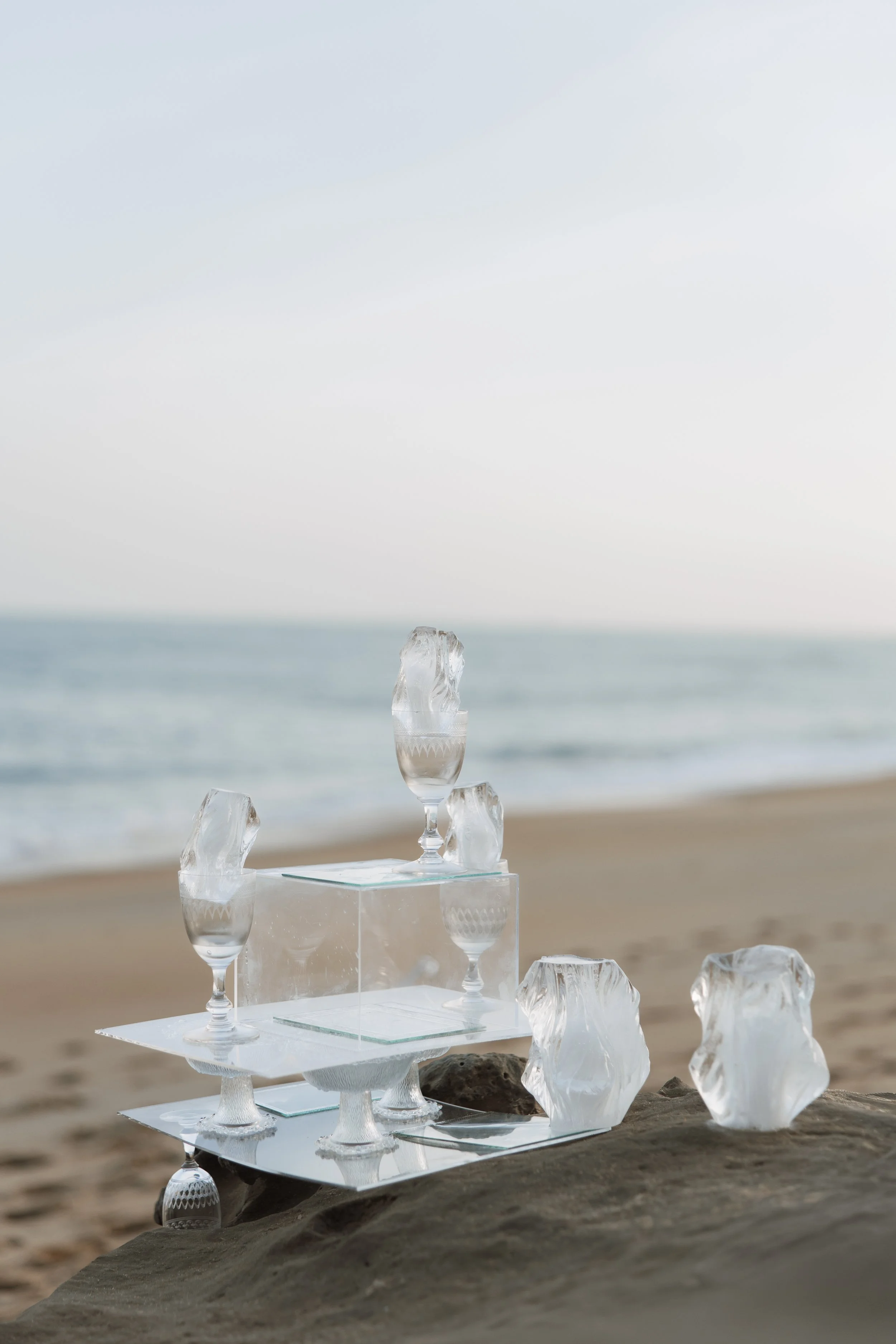 Editorial wedding detail of sculptural ice glassware displayed on a French beach, captured with a soft, refined aesthetic