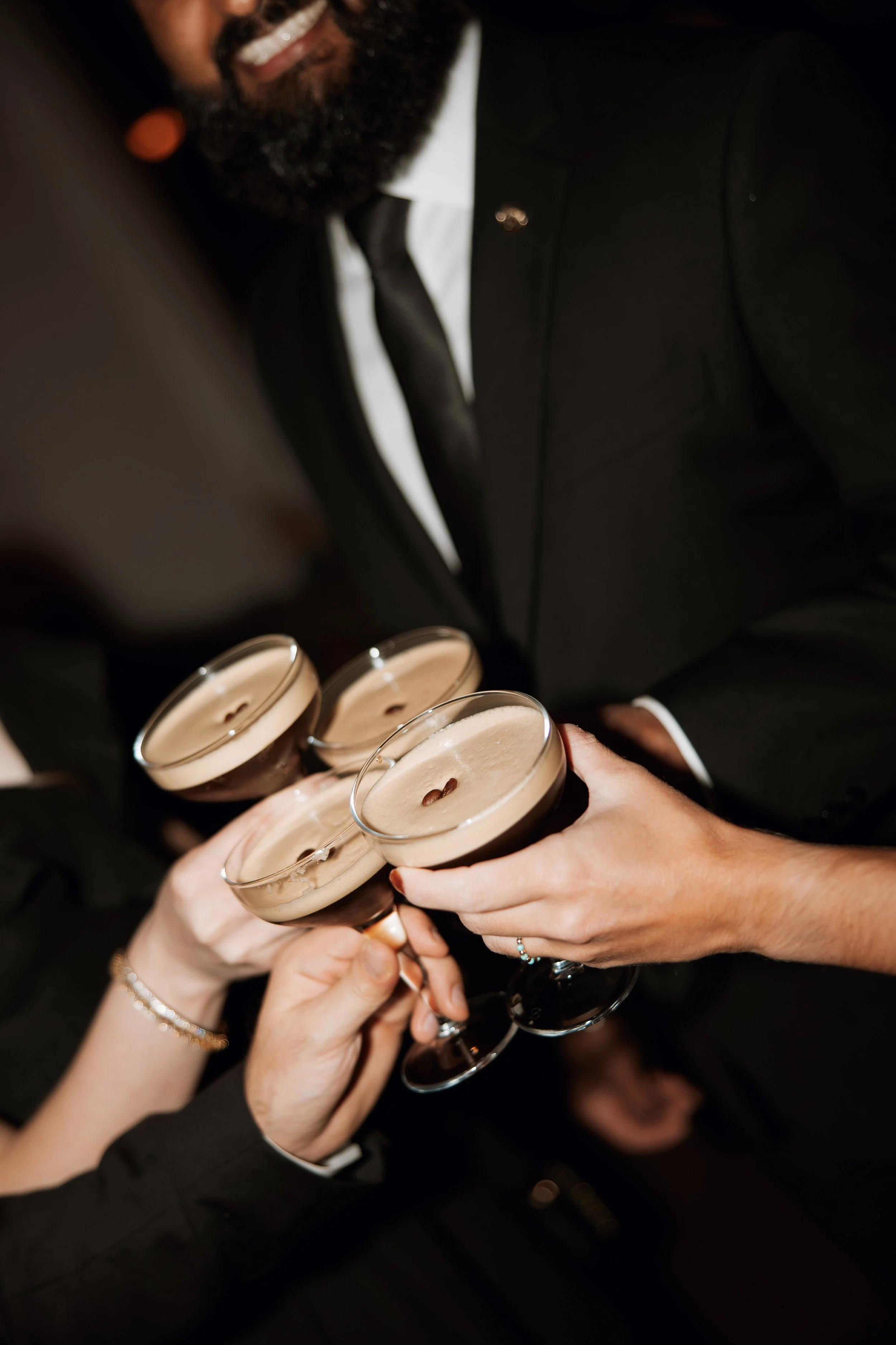 People in formal attire clinking glasses of coffee with coffee beans on top in a toast.