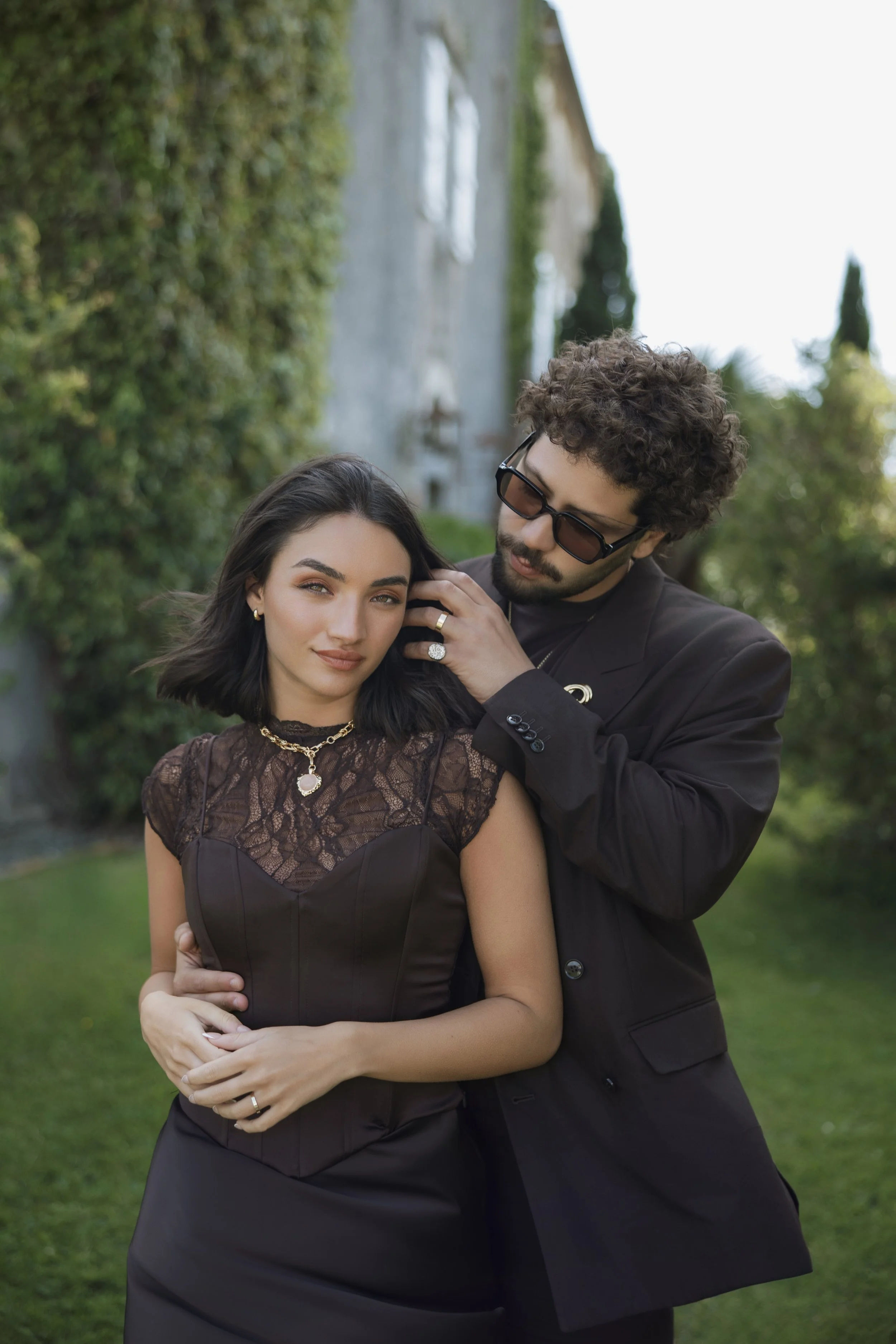 Editorial pre-wedding portrait of a stylish couple in Biarritz, with the groom adjusting the bride’s hair, captured in a relaxed, fashion-inspired setting.