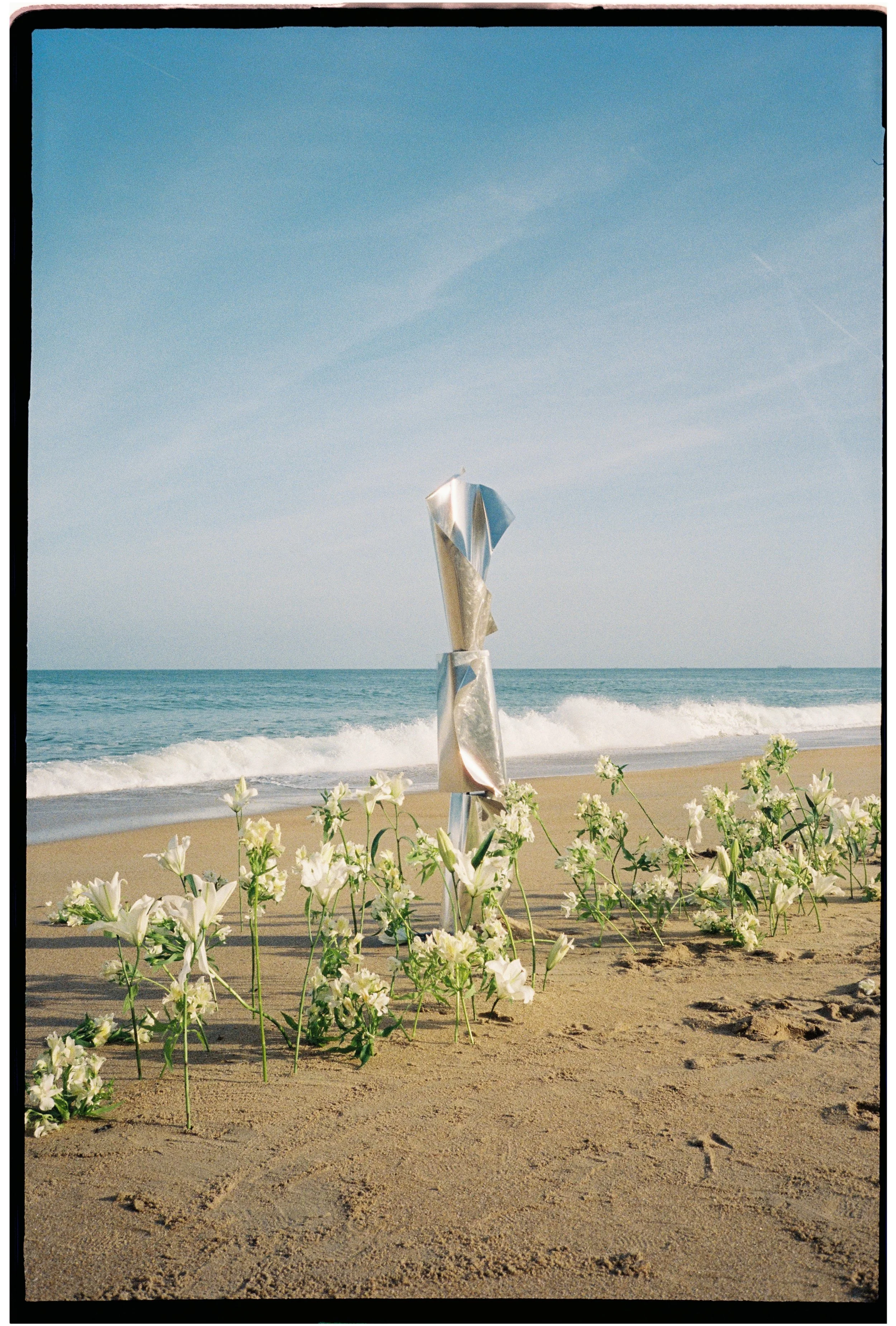 Editorial beach wedding inspiration featuring white flowers on the shoreline, photographed on 35mm film with a natural coastal aesthetic