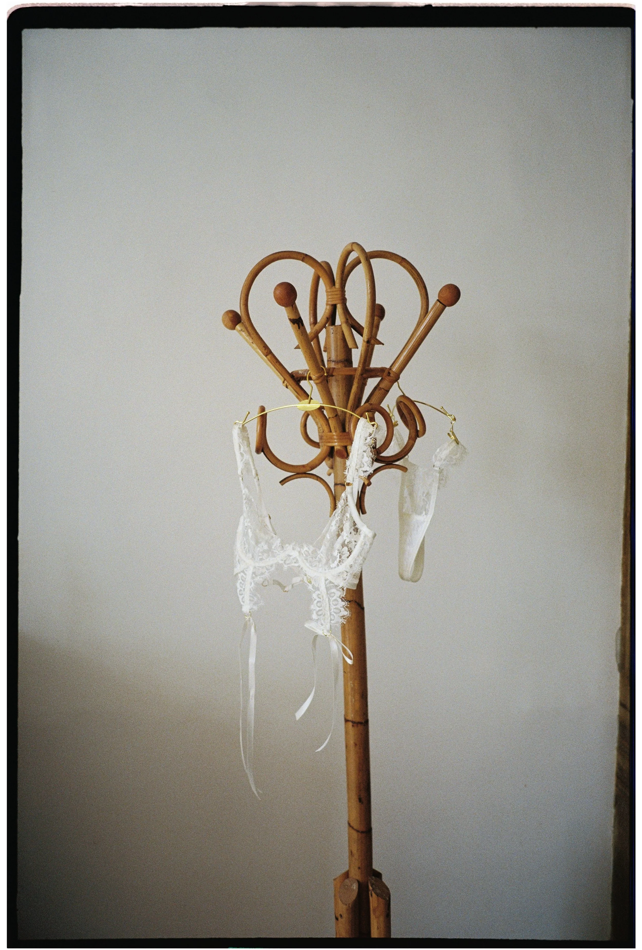 Bridal lingerie hanging on a vintage rattan coat stand in soft natural light, photographed on film.