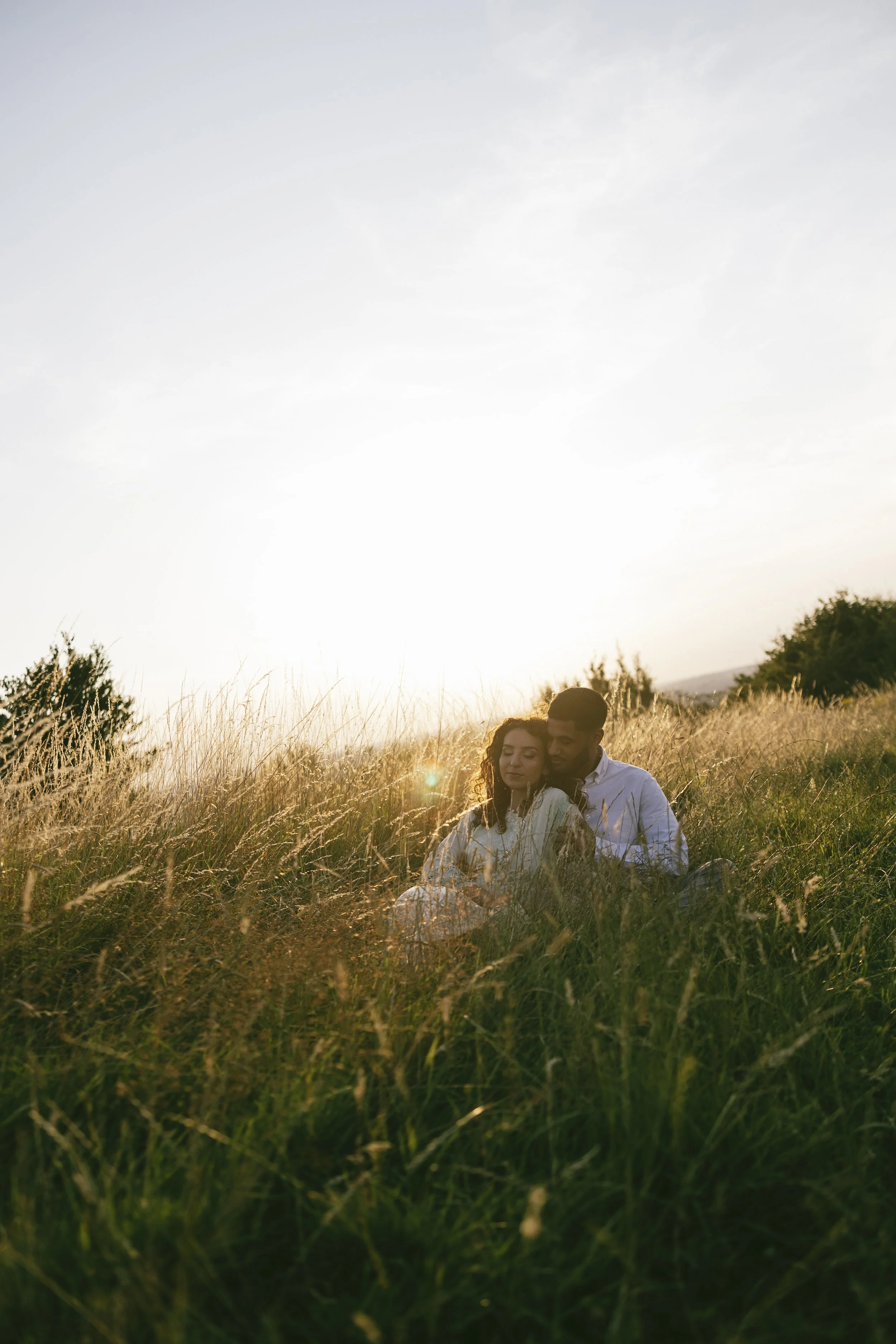 Romantic pre-wedding photoshoot showing a couple sitting together in soft golden evening light