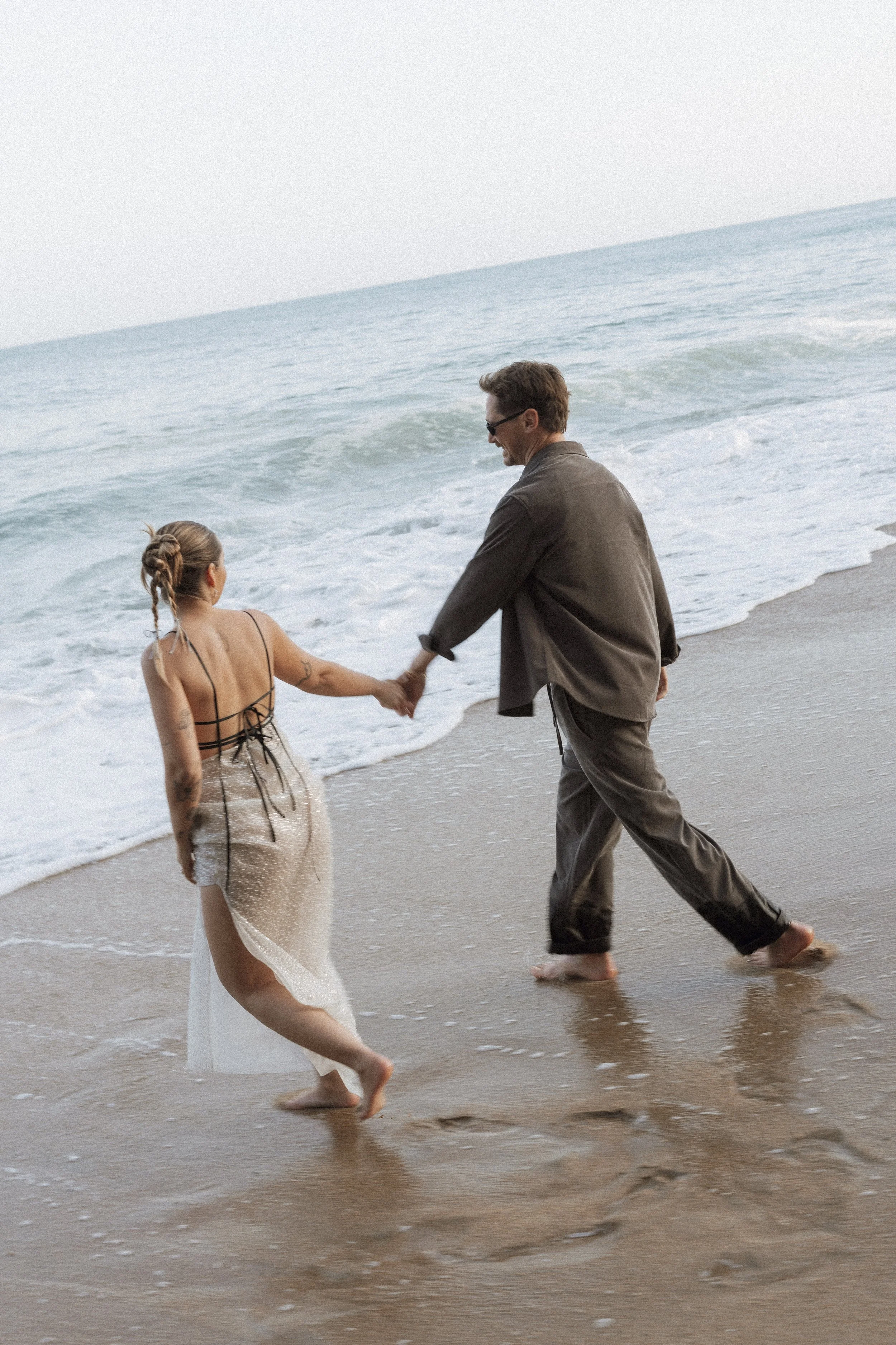 Couple walking hand in hand along the shoreline, captured in an editorial, fashion-inspired destination wedding photography style