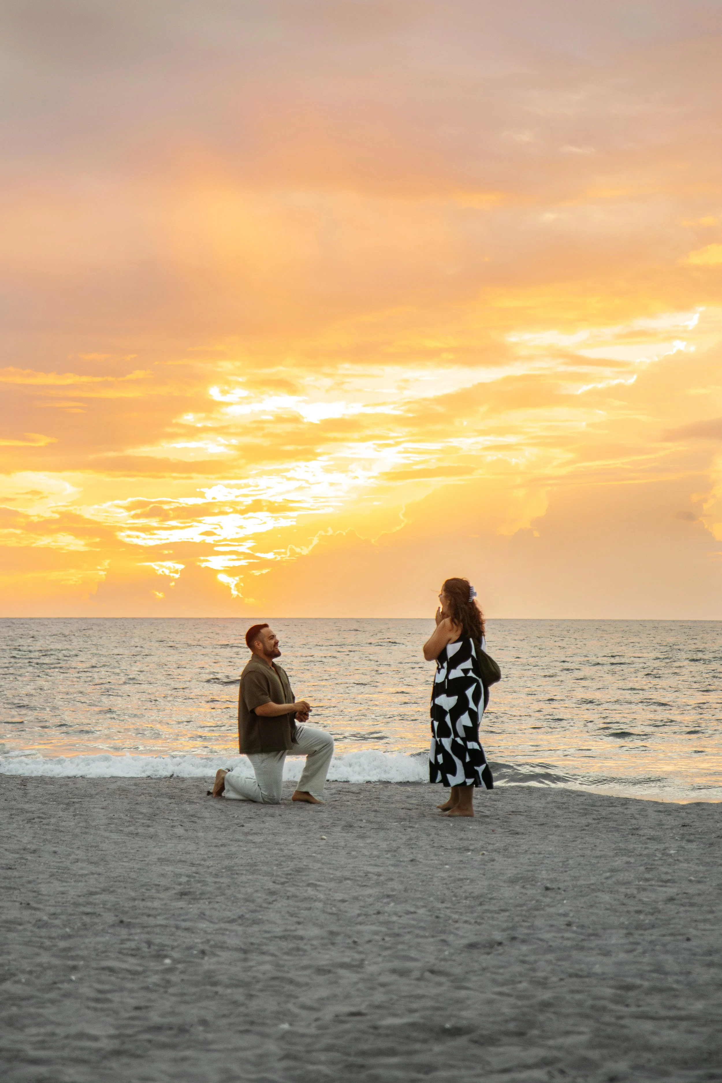 A man proposing marriage to a woman on the beach at sunrise, with the ocean in the background during a Romantic Beach Couples Photography Session and surprise beach proposal. 