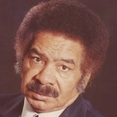Portrait of Sax Kari, form the author's personal collection, with an afro hairstyle and a mustache, wearing a dark jacket and a white shirt.