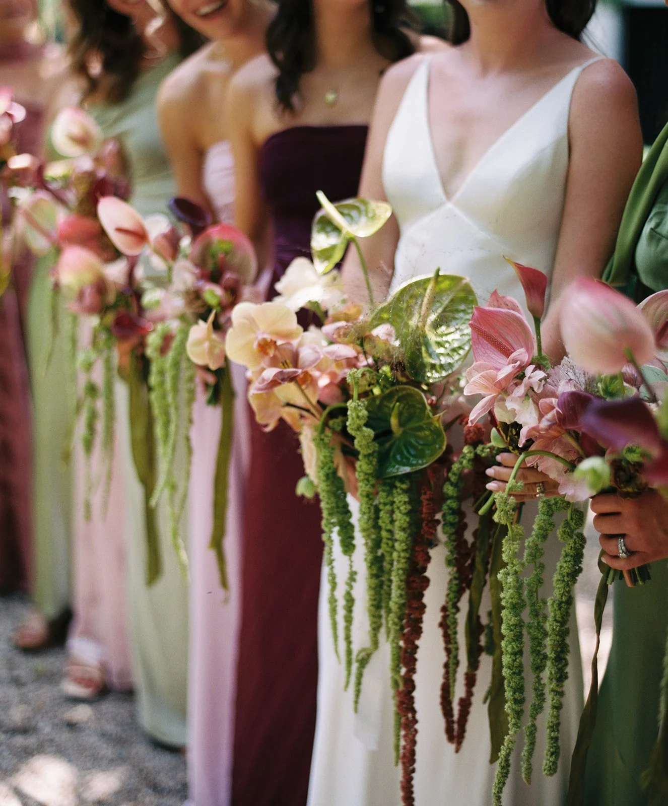 Line of women holding bridal bouquets with pink and green flowers at an outdoor wedding.