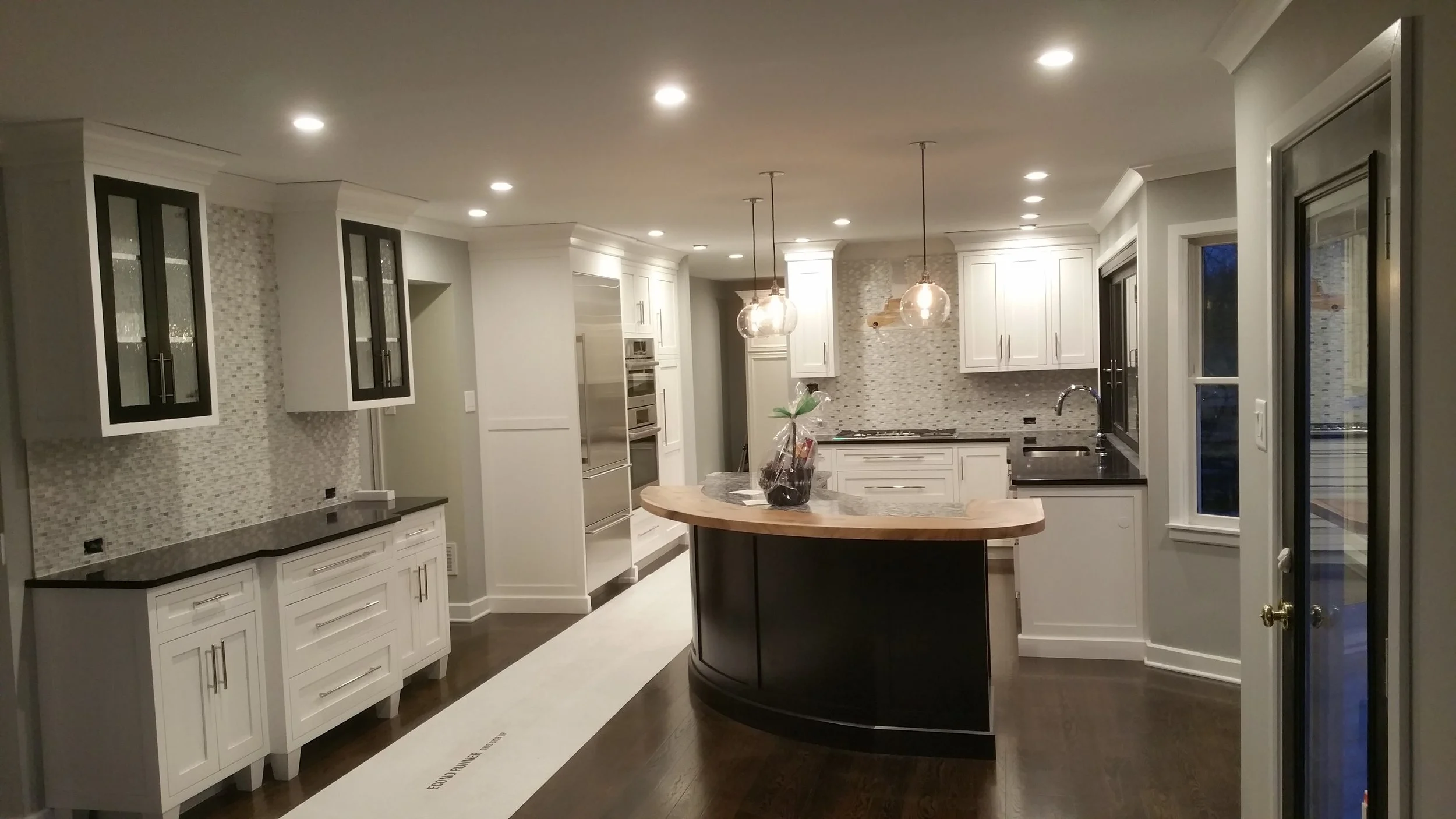 Modern kitchen with white cabinets, black countertops, mosaic tile backsplash, island with wooden top, pendant lights, and stainless steel appliances.