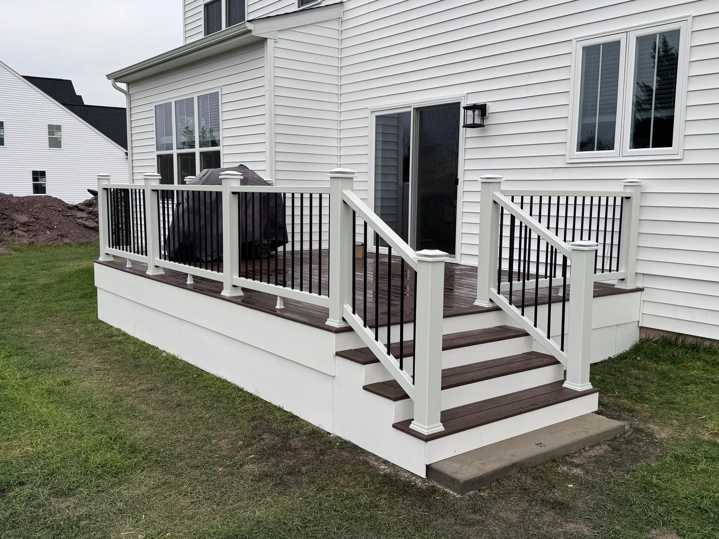 Backyard deck with stairs, white railing with black spindles, sliding glass door, and outdoor wall light